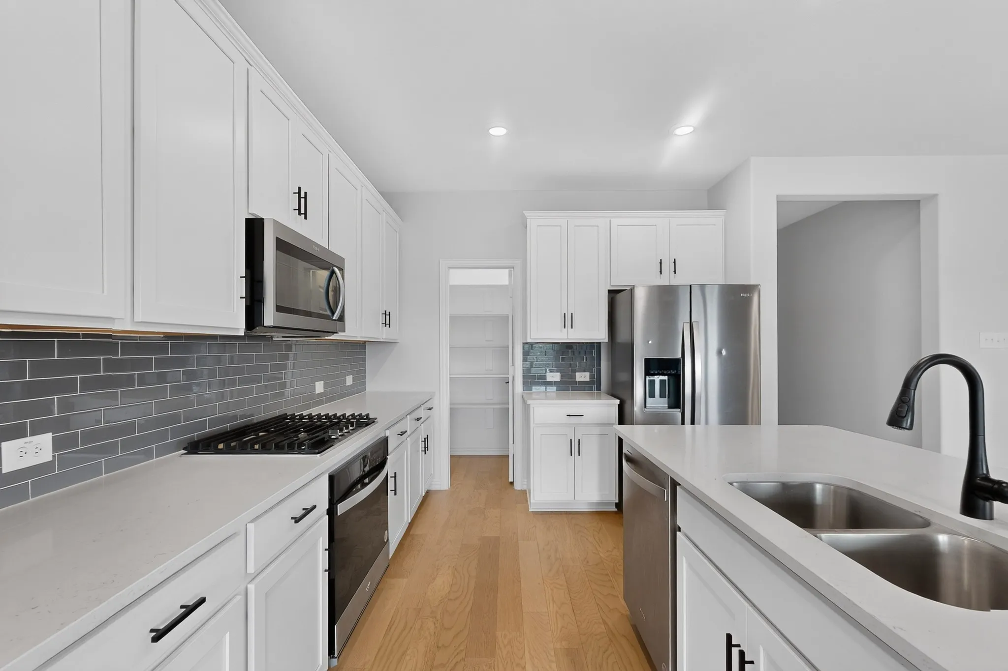 Kitchen featuring light wood-finish flooring, white cabinetry, integrated stainless steel appliances, a gray subway tile backsplash, and light-toned countertops