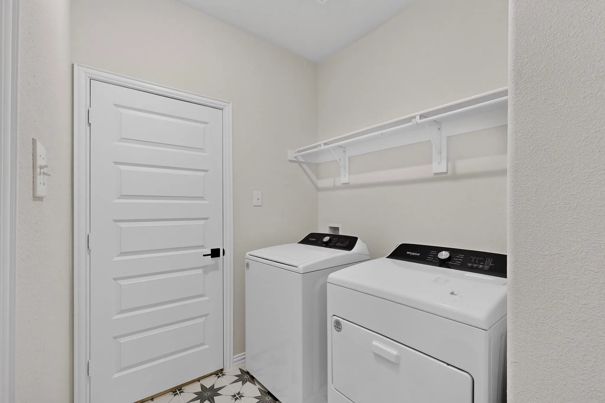 Laundry room with patterned floor tile, white wall shelving, and a horizontal panel door with matte black hardware