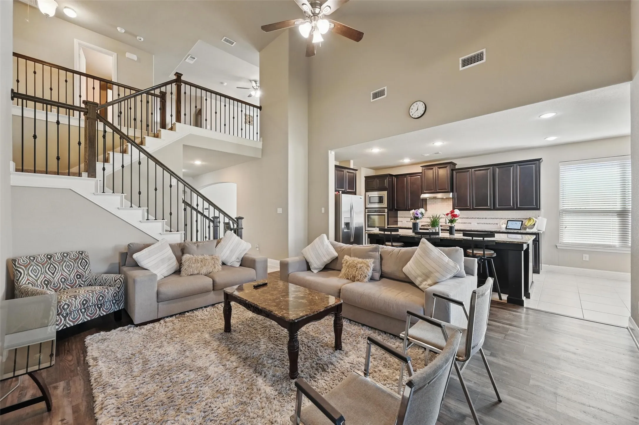 Two-story living area with high ceilings, wood-finish flooring, and a staircase featuring wrought iron balusters