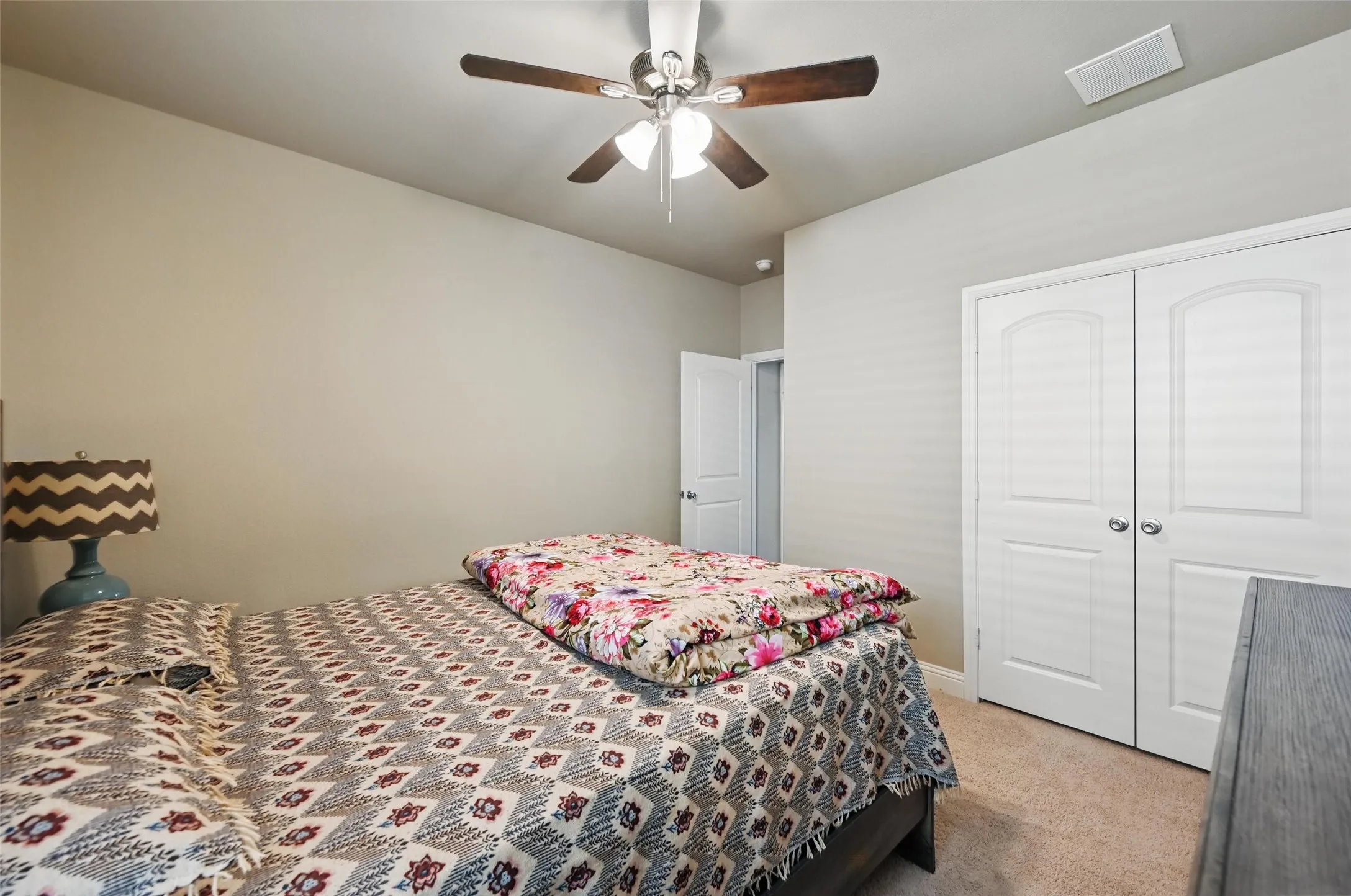 Neutral tone walls, carpet flooring, a ceiling fan with integrated lighting, and white bi-fold closet doors