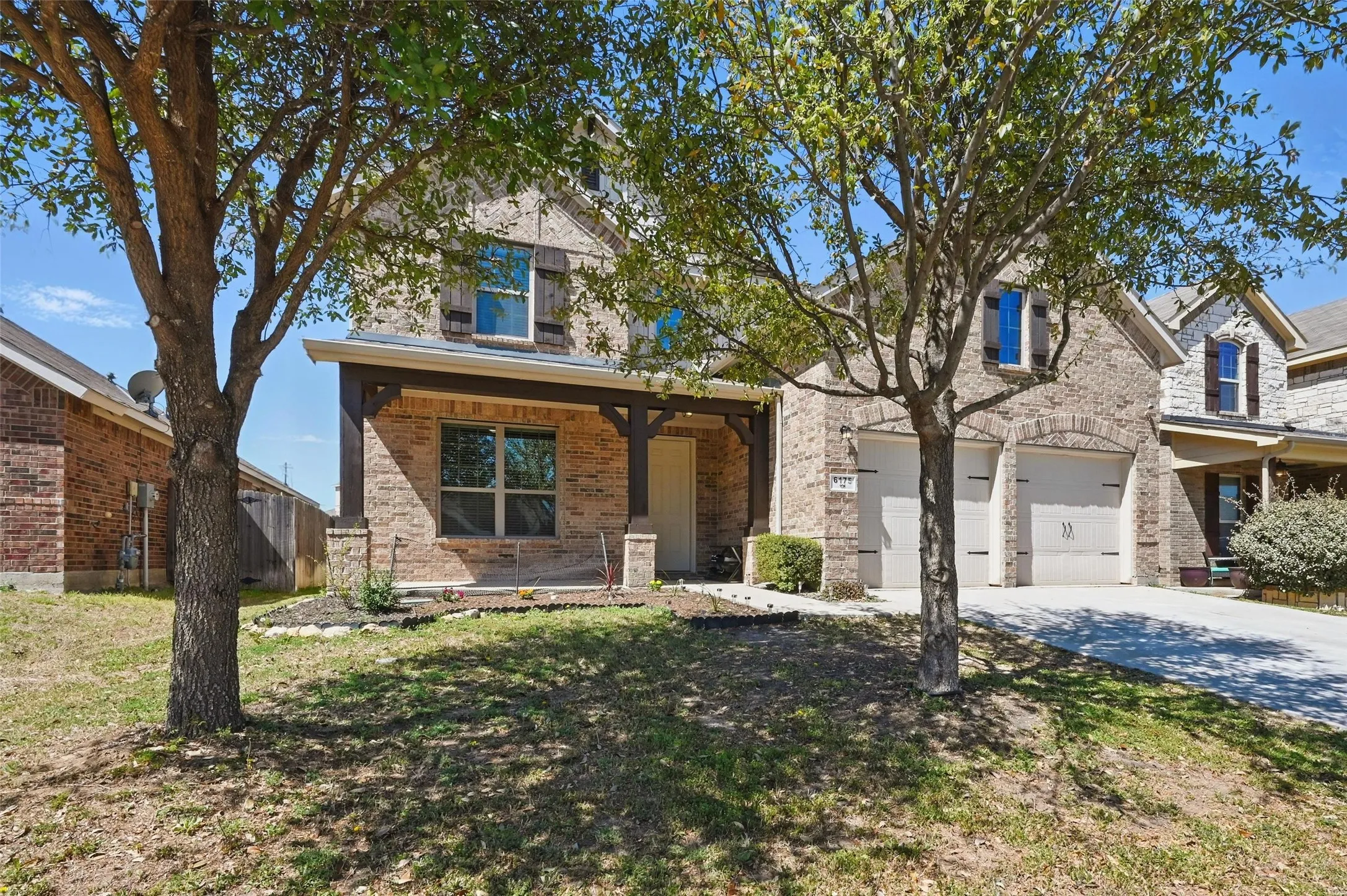 Brick facade home with a covered front porch, dark wood columns, decorative window shutters, and an attached two-car garage