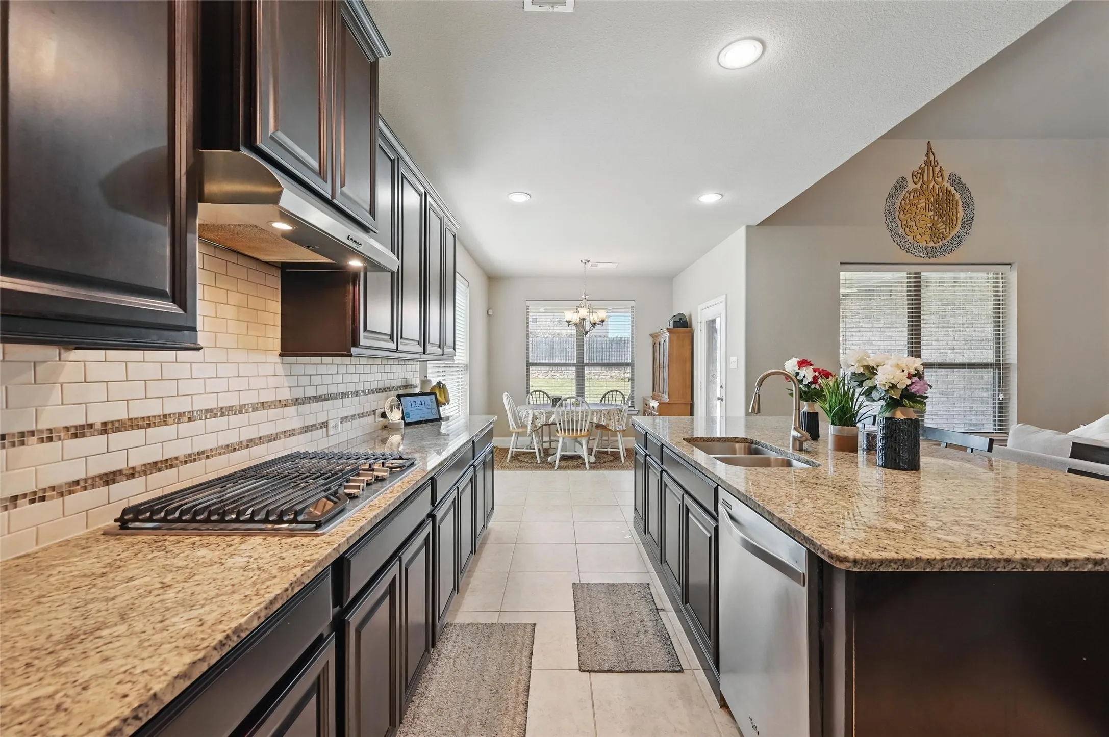 Kitchen featuring dark wood cabinetry, light granite countertops, a tile backsplash with decorative accents, a built-in gas range, and a stainless steel sink