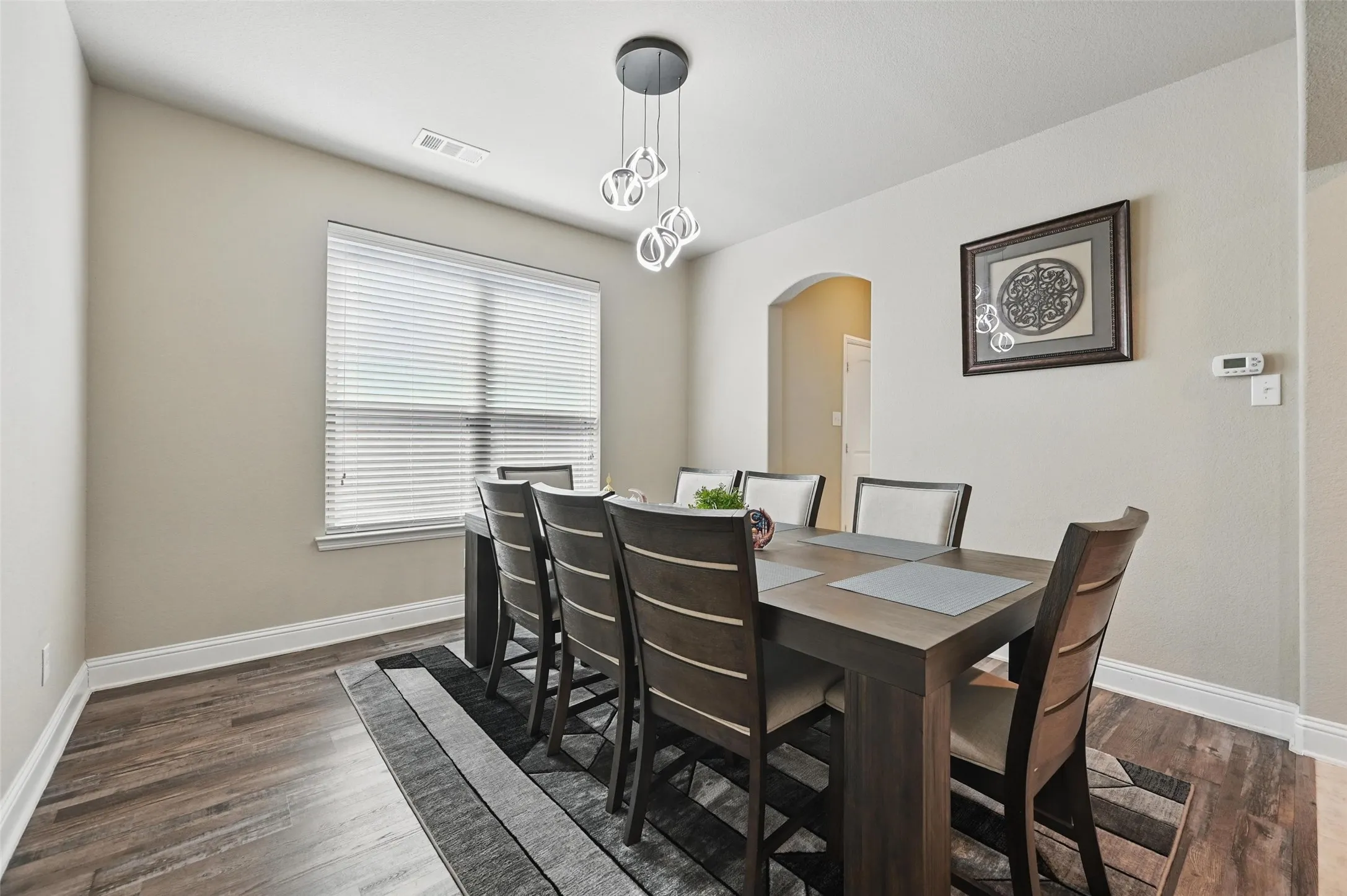 Wood-finish flooring, recessed window with blinds, arched doorway, and a contemporary chandelier