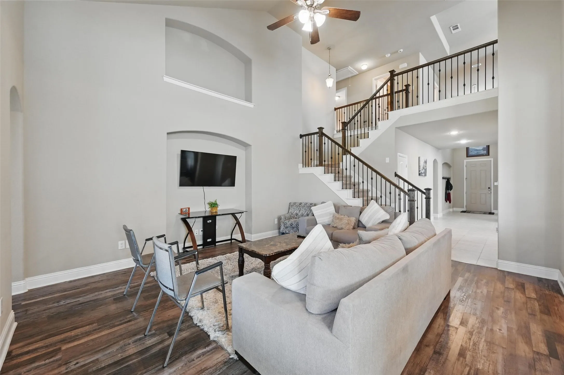 Two-story living area with high ceilings, wood-finish flooring, and a ceiling fan