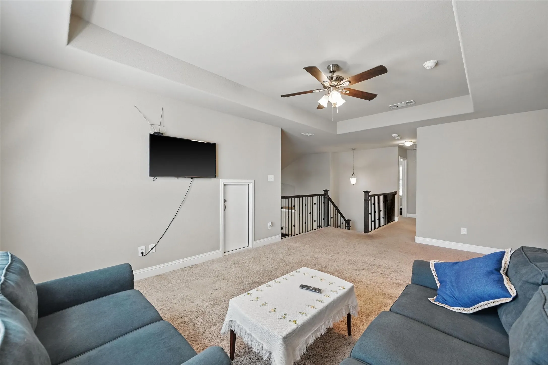 Tray ceiling with a ceiling fan, carpeted flooring, and dark wood newel posts with iron balusters