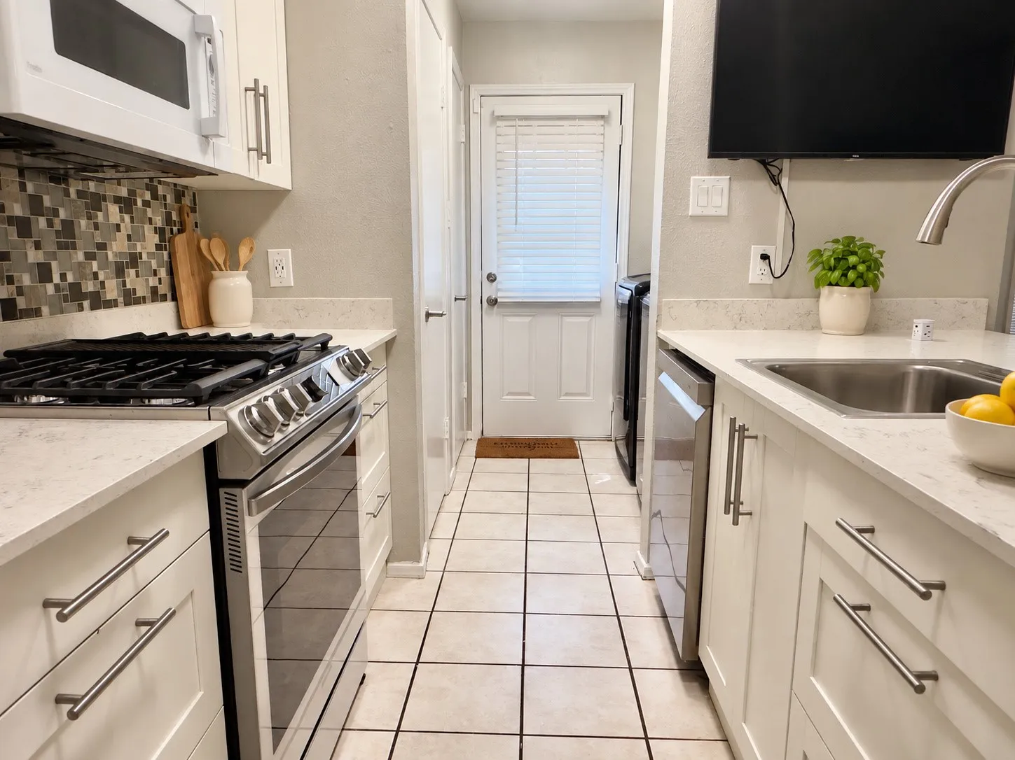 Contemporary kitchen featuring white cabinetry, light-toned countertops, a mosaic tile backsplash, stainless steel appliances, and tile flooring