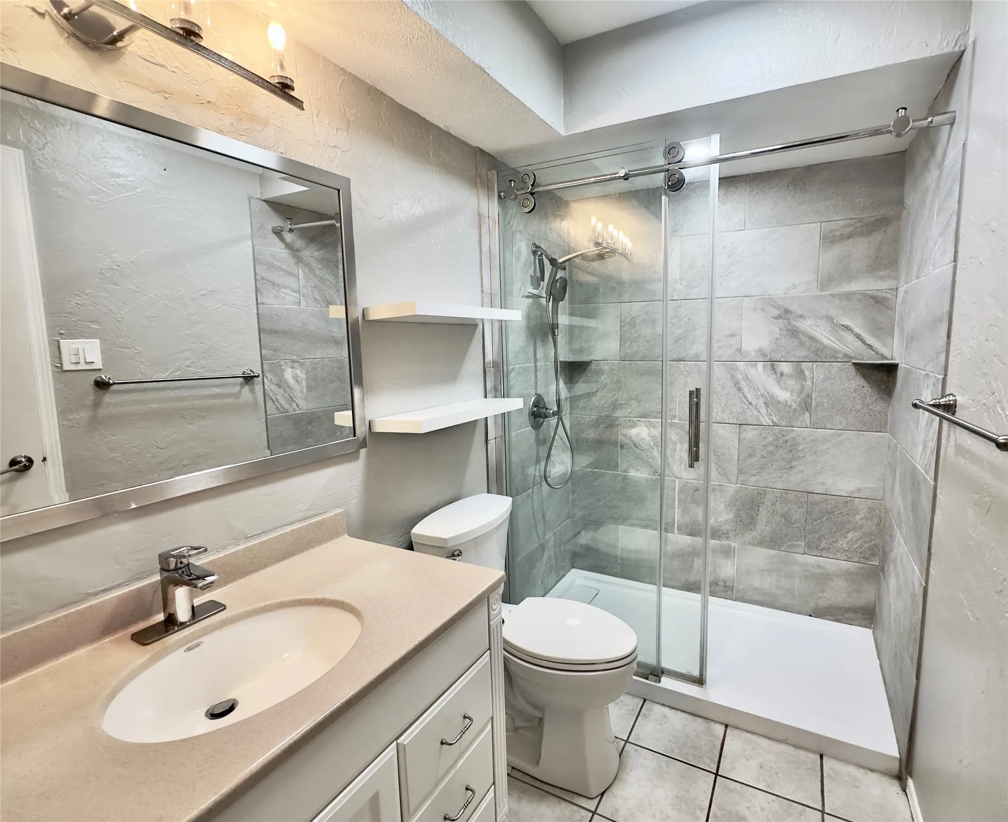 Contemporary look and feel in the Primary Bathroom- featuring a framed mirror, floating shelves, a walk-in shower with sliding glass doors, a built-in shower niche, and extensive tile work