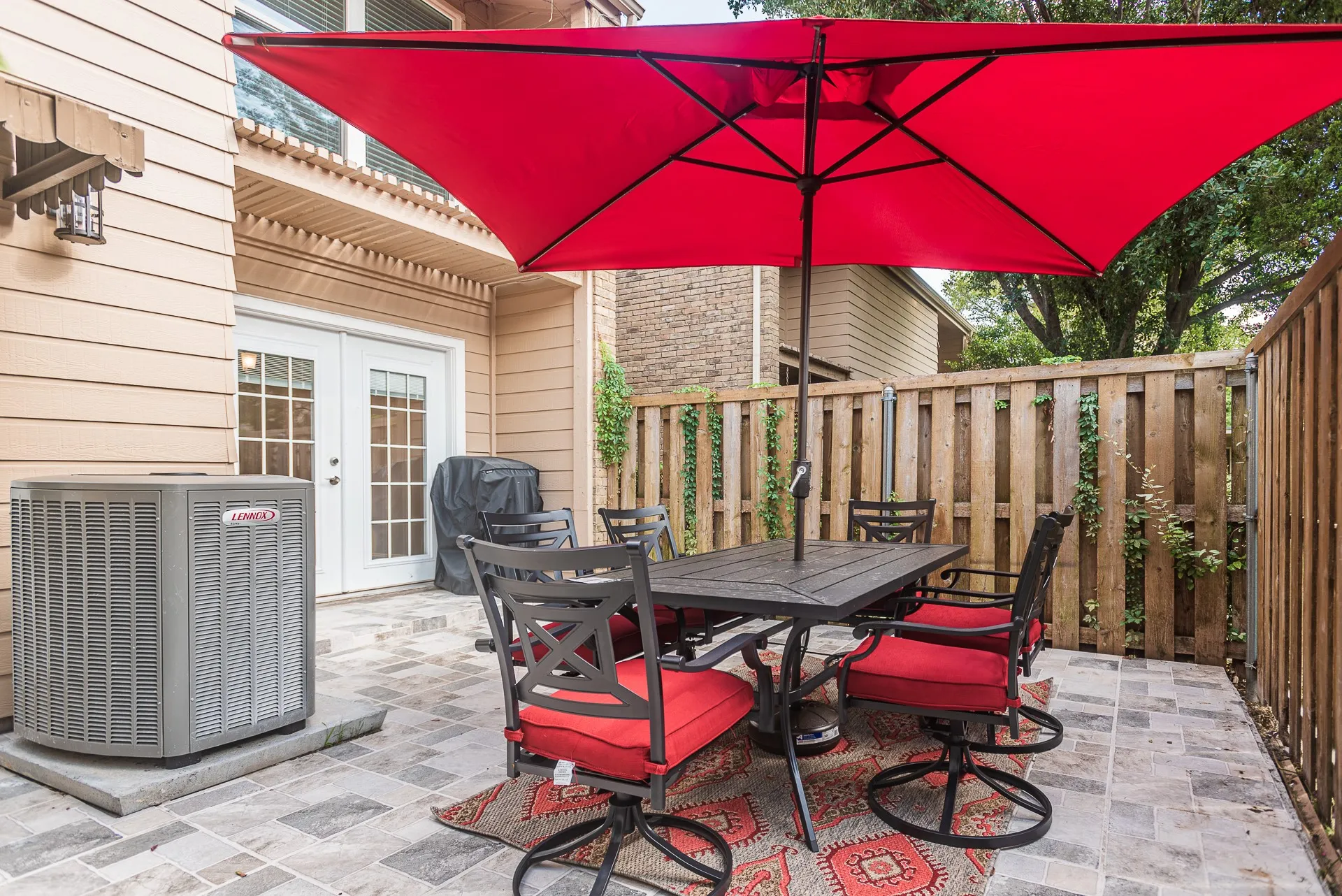 Paved patio with multi-toned stone pavers, wood privacy fence, and double glass-paned, grill, outdoor TV and Patio set