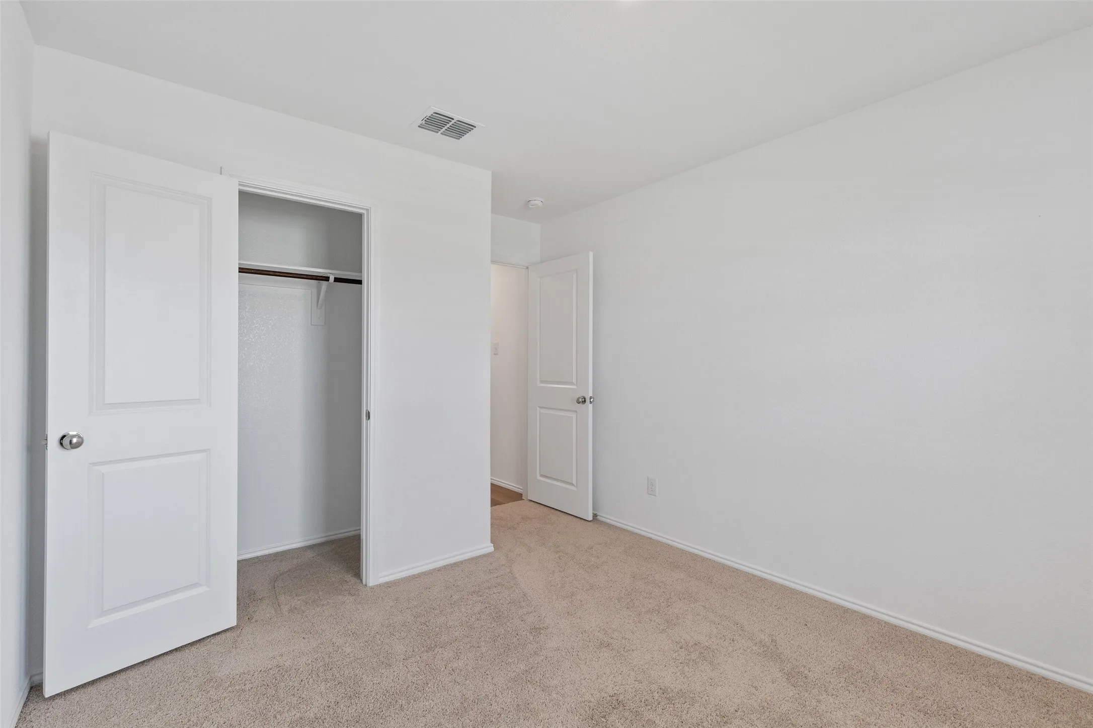Carpeted flooring, white walls, and a built-in closet with shelving and hanging rod