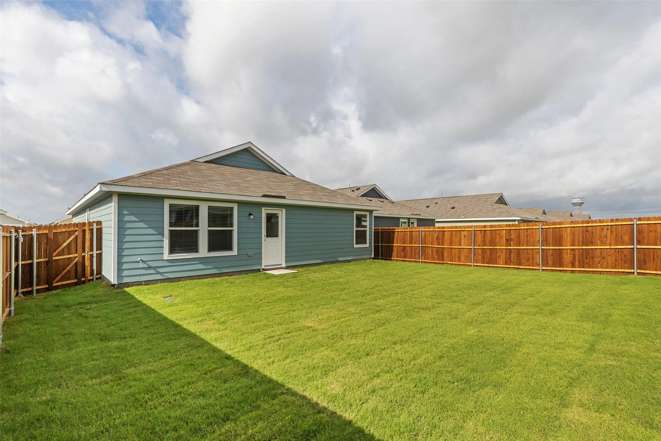 Expansive backyard featuring a manicured lawn, full wood-plank fencing, and a rear exterior with siding