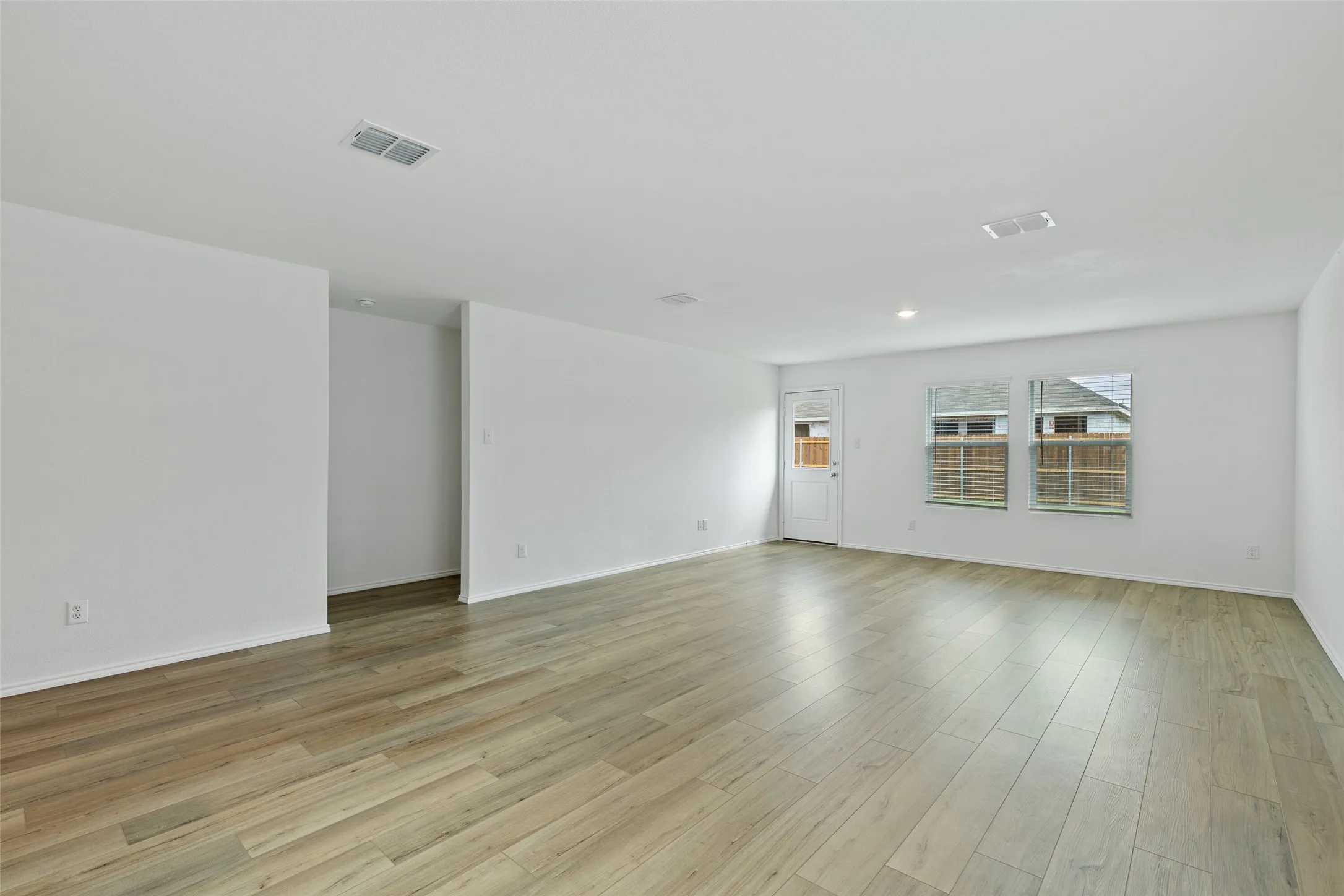 Expansive room featuring wood-finish flooring, white walls, multiple windows, and recessed lighting