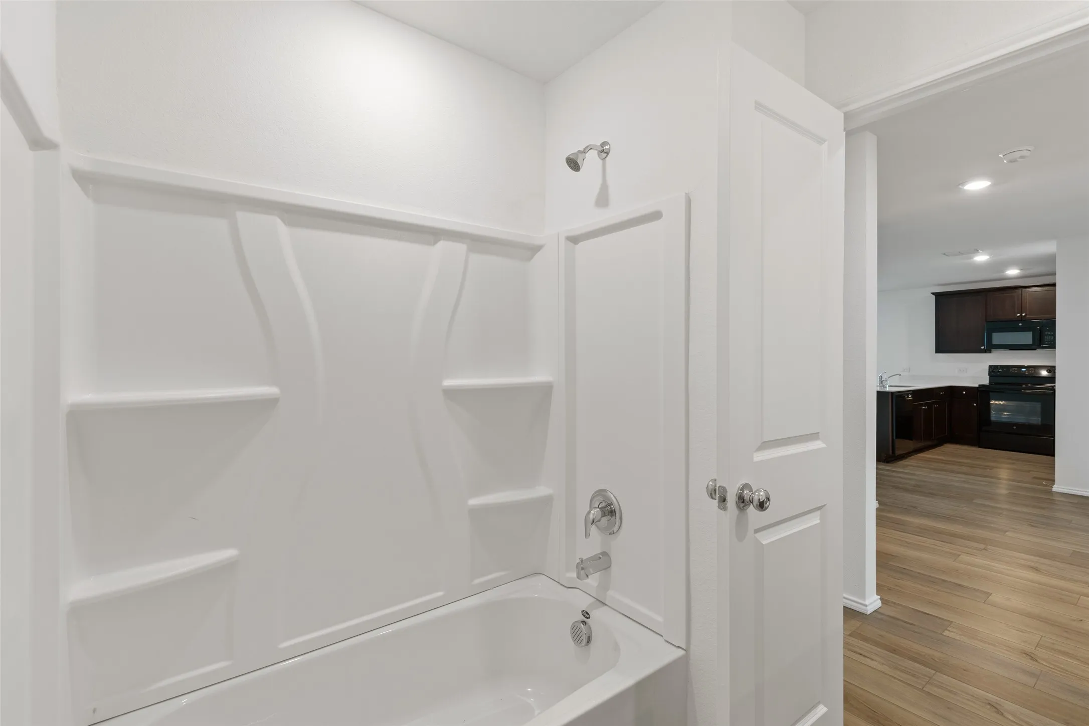 White shower-tub combination featuring integrated shelving and chrome fixtures