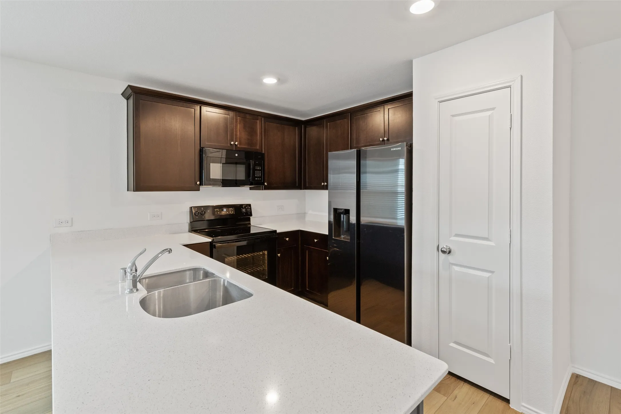 Kitchen featuring dark wood cabinetry, light-toned countertops, stainless steel sink, and wood-finish flooring