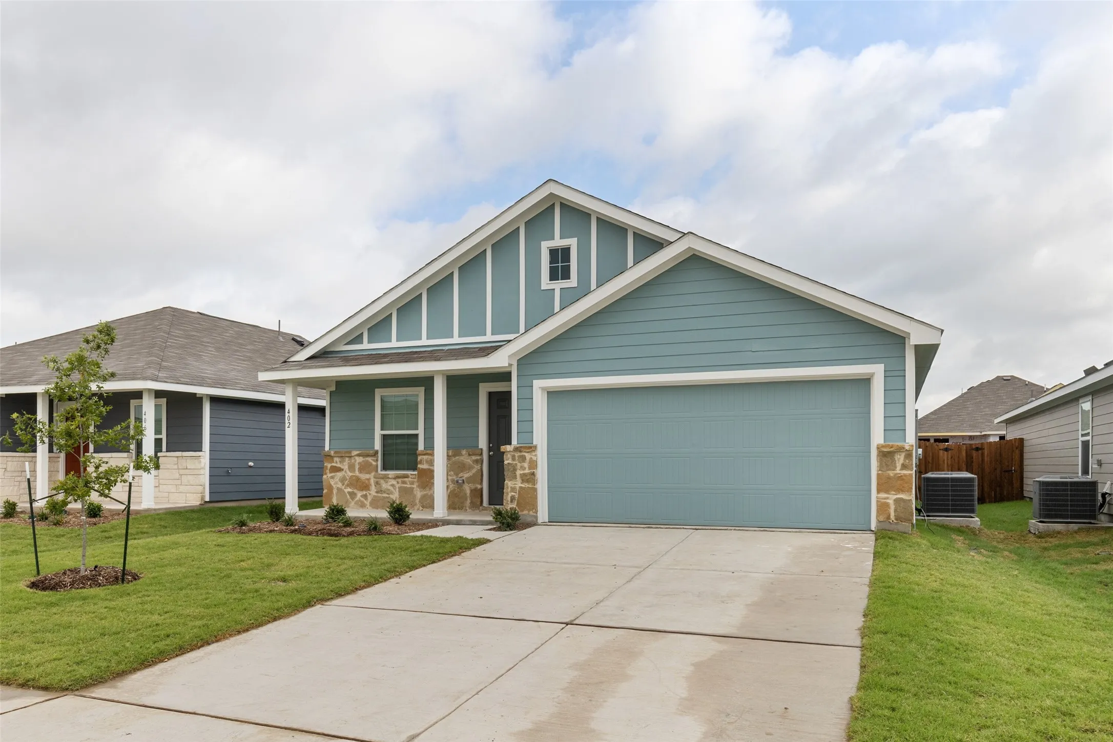 Blue siding exterior with stone accents, a covered front porch, and an attached two-car garage