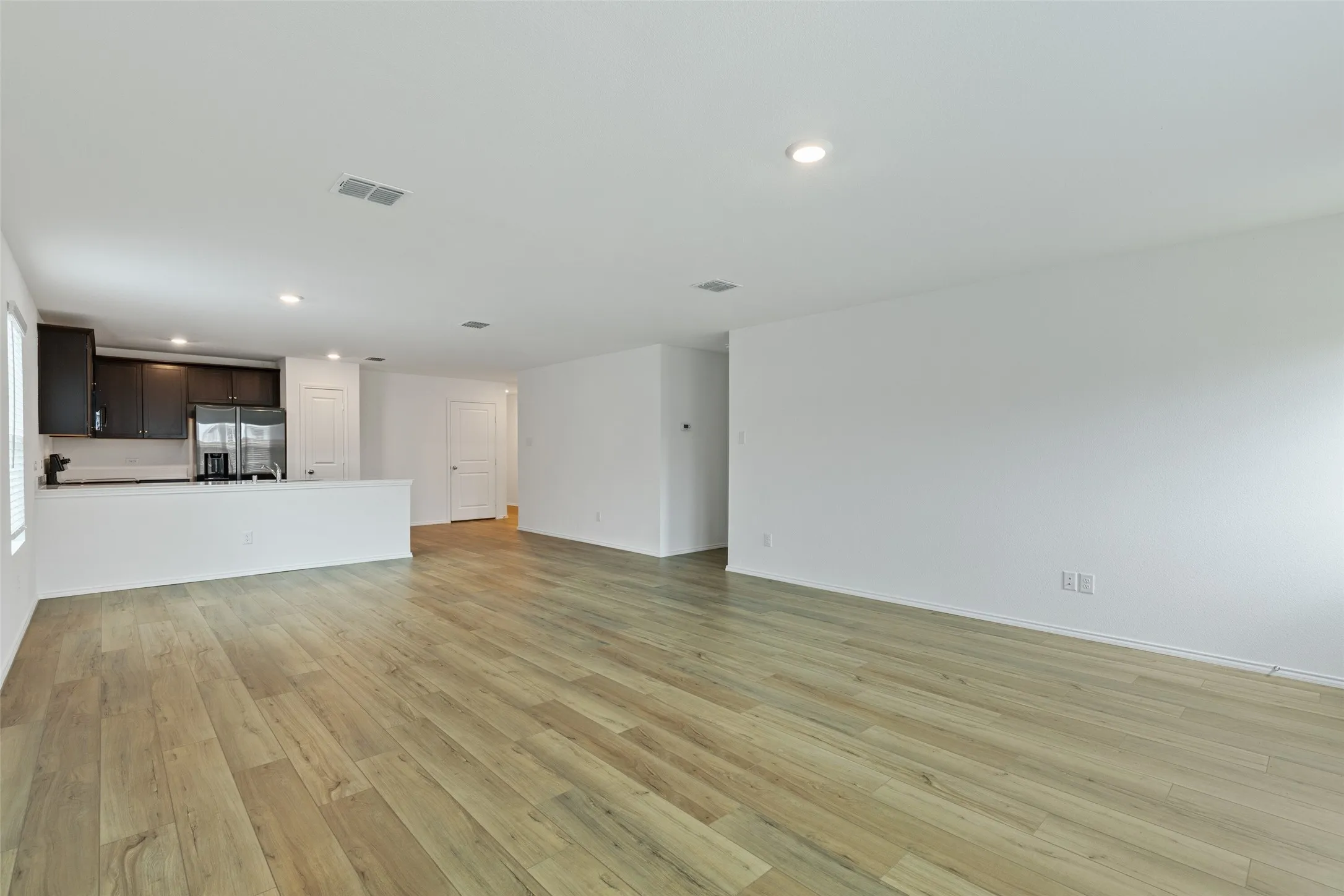 Wood-finish flooring throughout, recessed lighting, and a kitchen featuring dark wood cabinetry, white countertops, and stainless steel appliances