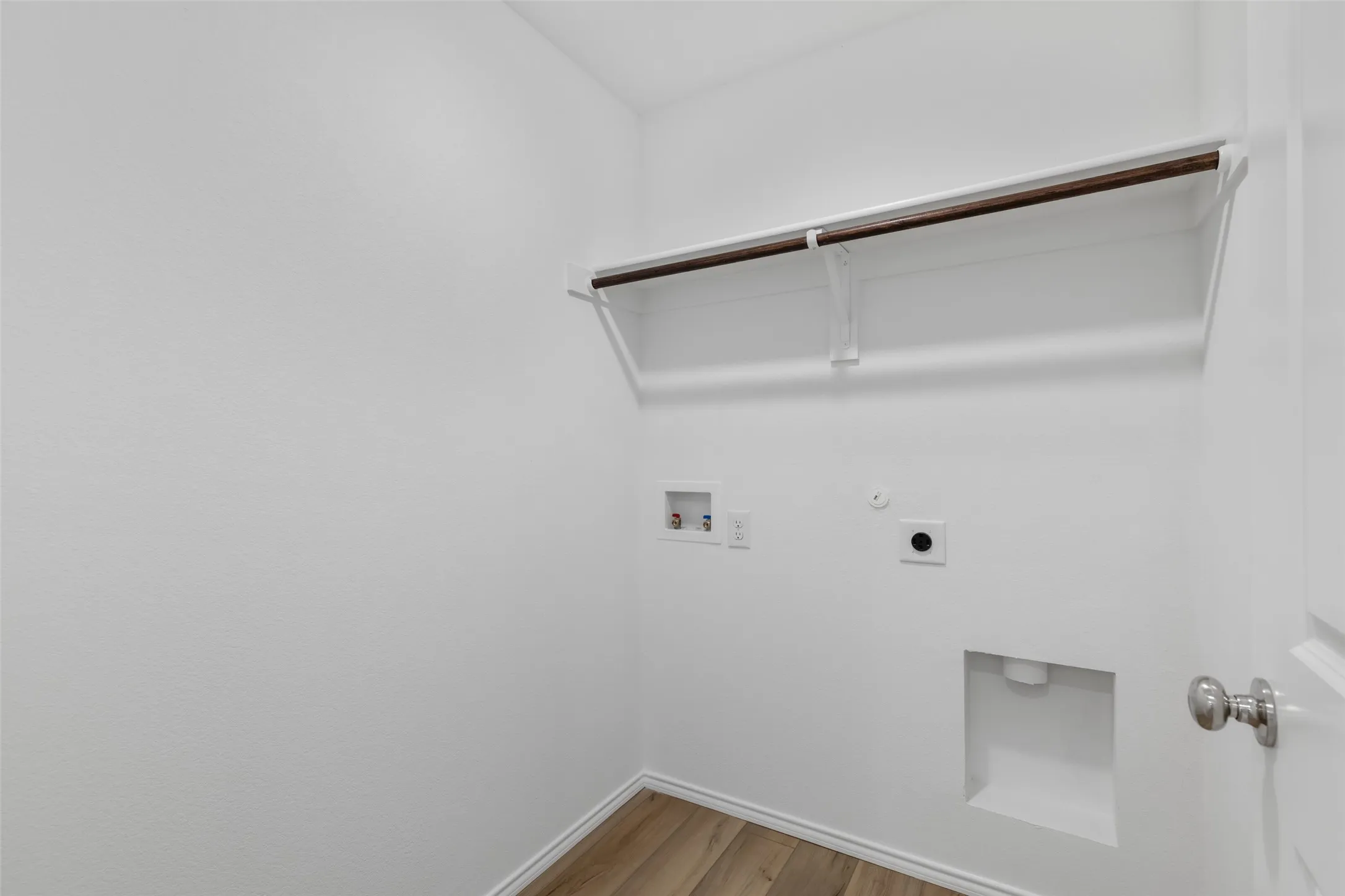 Laundry area featuring white walls, wood-finish flooring, a clothes hanging rod, and appliance hookups