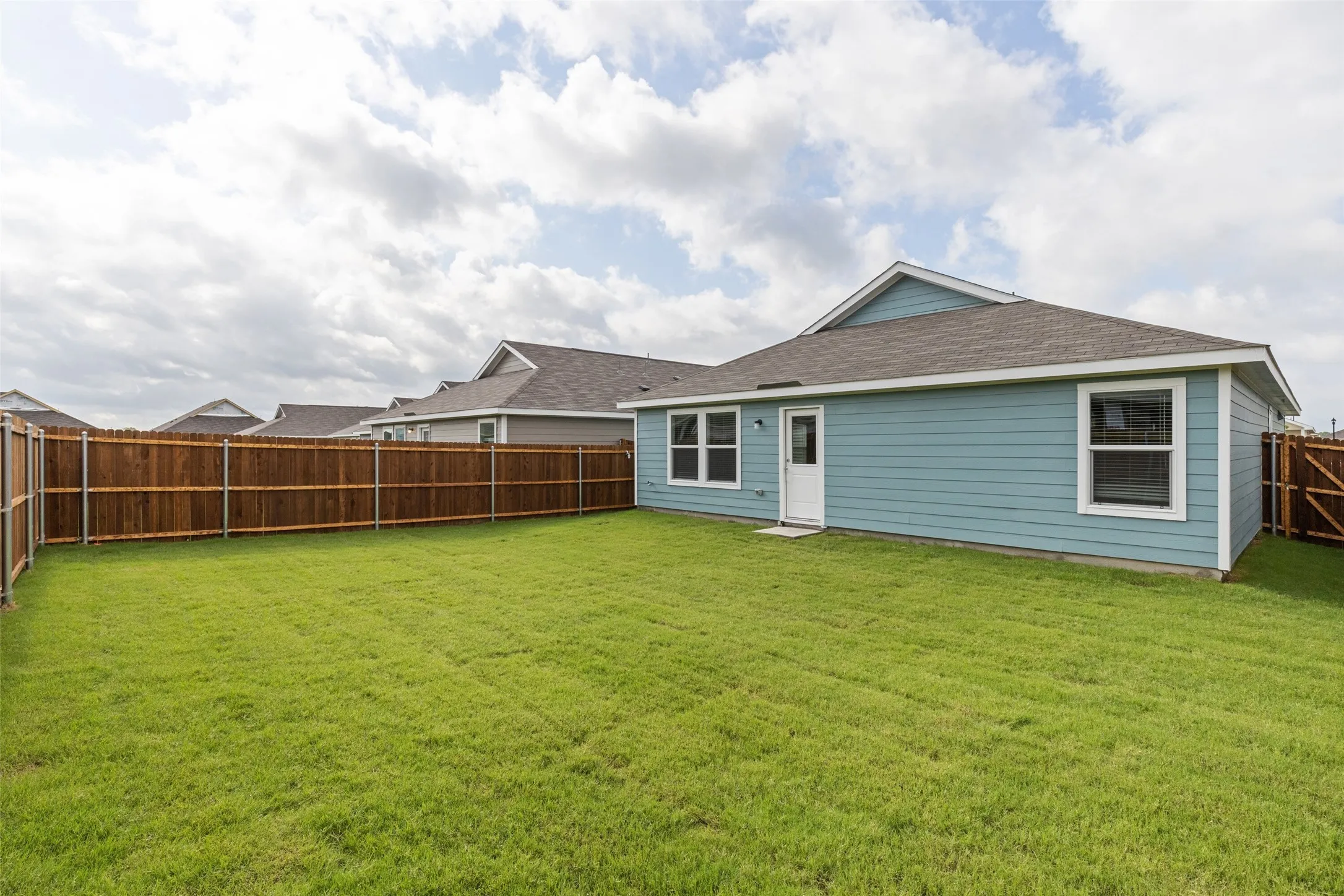 Spacious backyard featuring a manicured lawn, full wood privacy fencing, and light blue siding