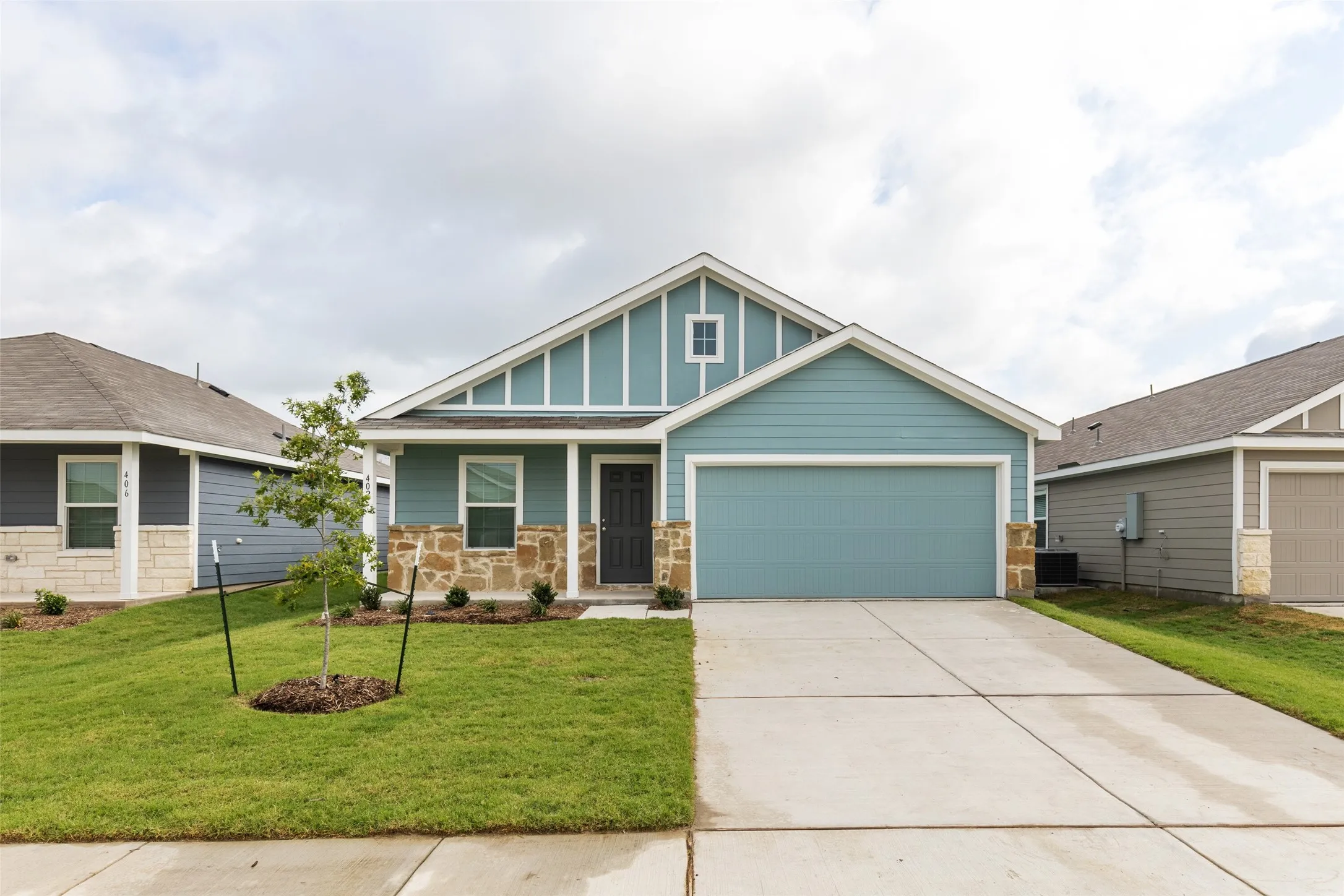 Modern exterior with a light blue facade, stone-finish accents, an attached garage, a dark entry door, and a concrete driveway