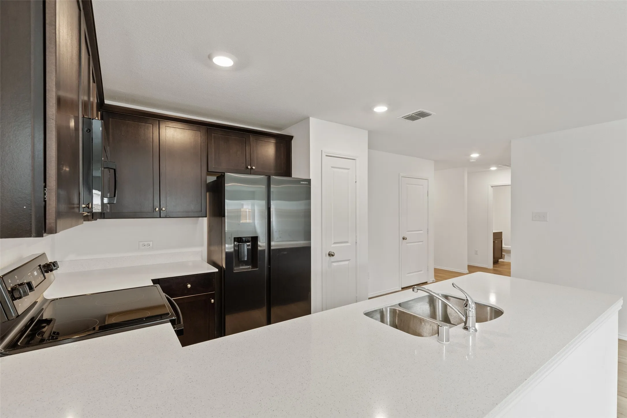 Kitchen featuring dark wood-finish cabinetry, white countertops, a stainless steel double basin sink, and recessed lighting