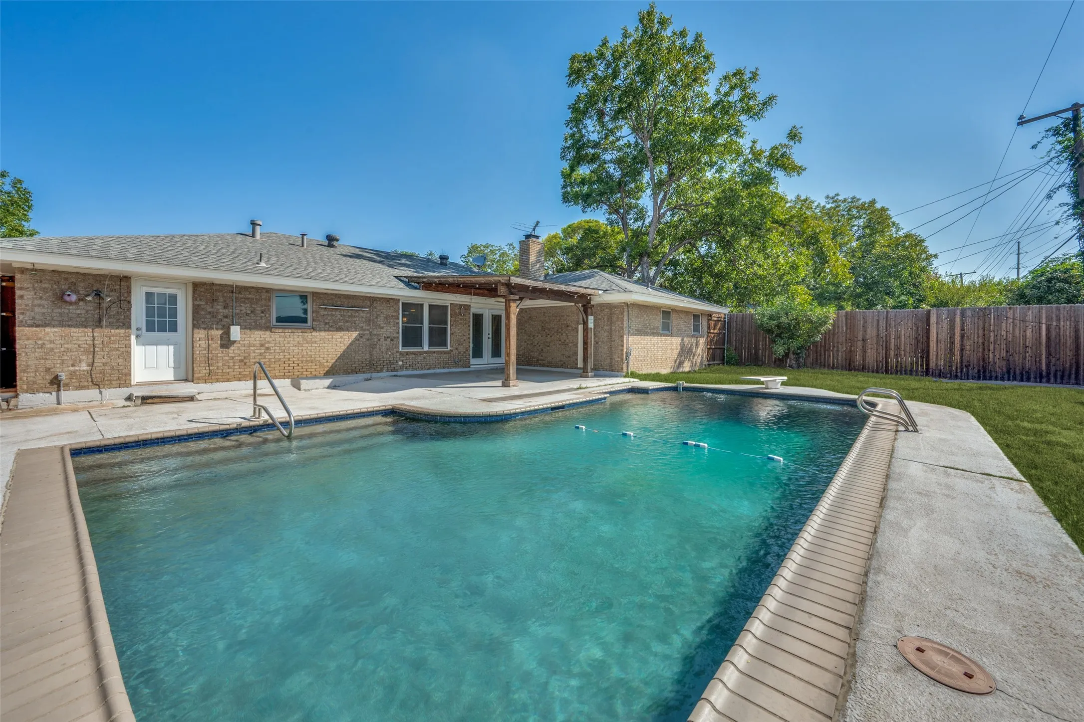 Expansive backyard featuring a rectangular swimming pool, concrete patio, a pergola structure, and a wood privacy fence