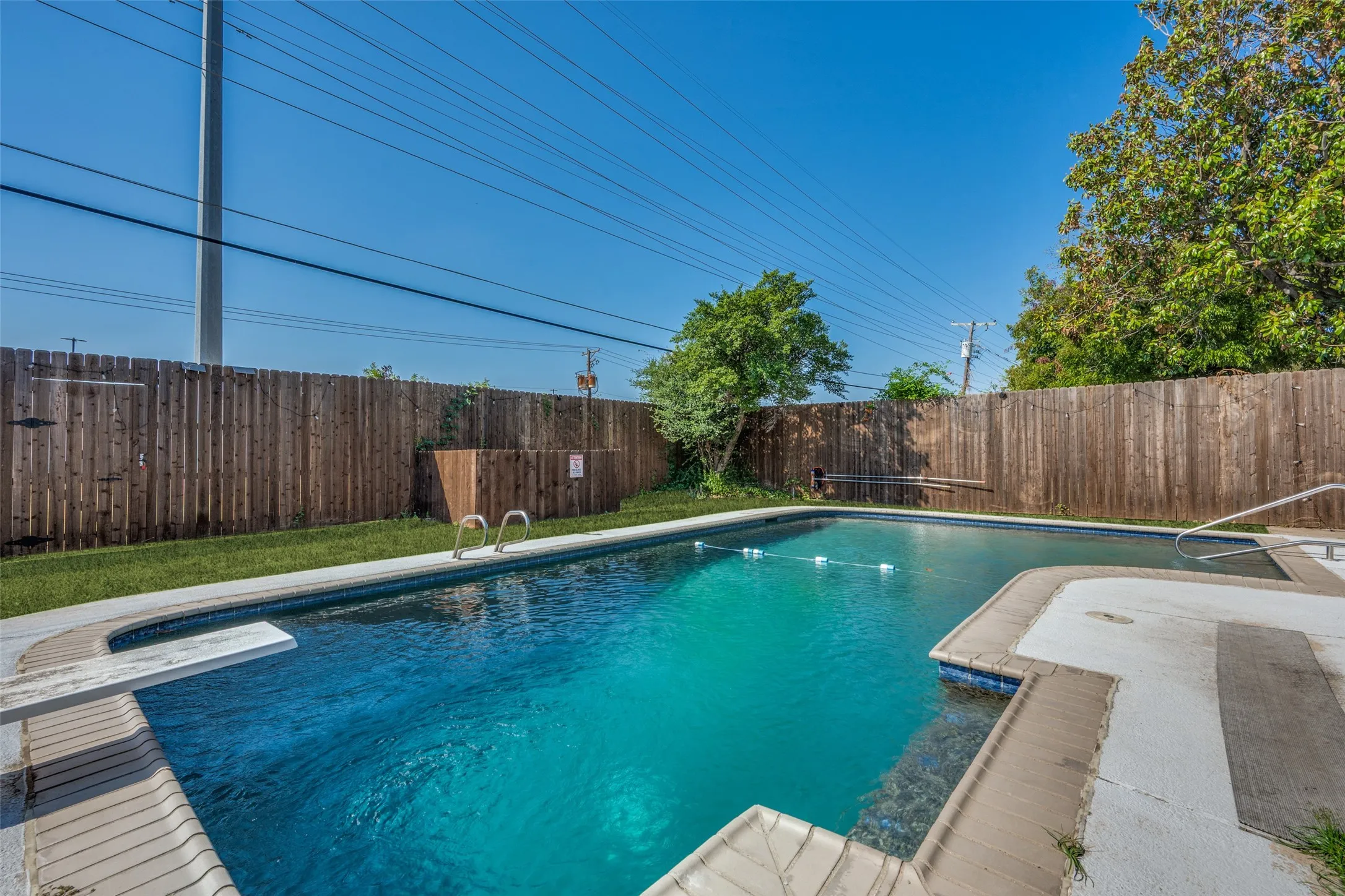 In-ground swimming pool with diving board, surrounded by a wood fence