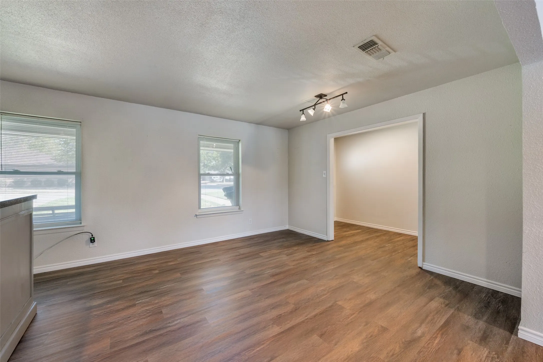 Wood-finish flooring throughout, light-colored walls, recessed ceiling, track lighting fixture, and window with blinds