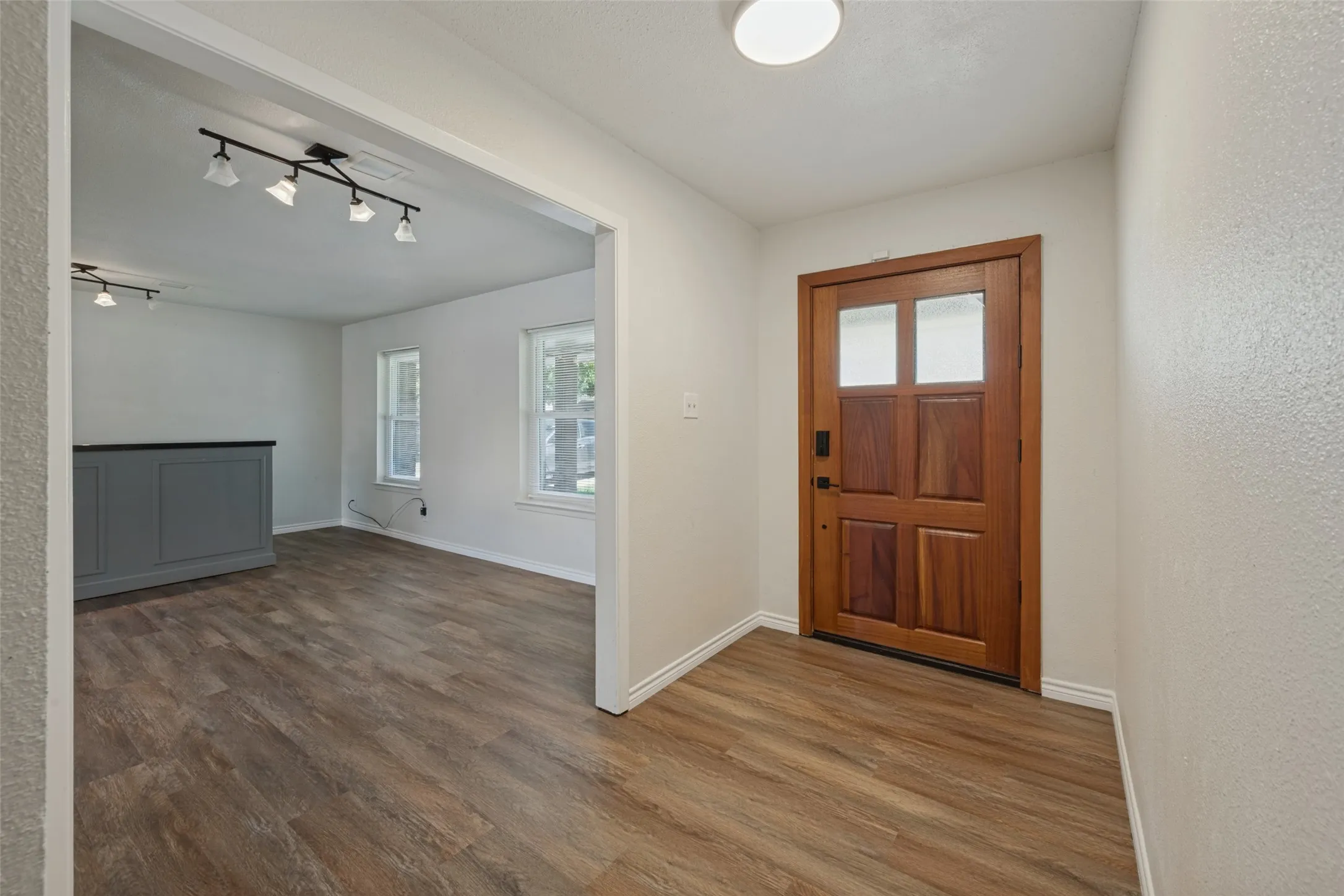 Wood-finish flooring throughout, solid wood entry door with frosted glass panels, and recessed ceiling lighting