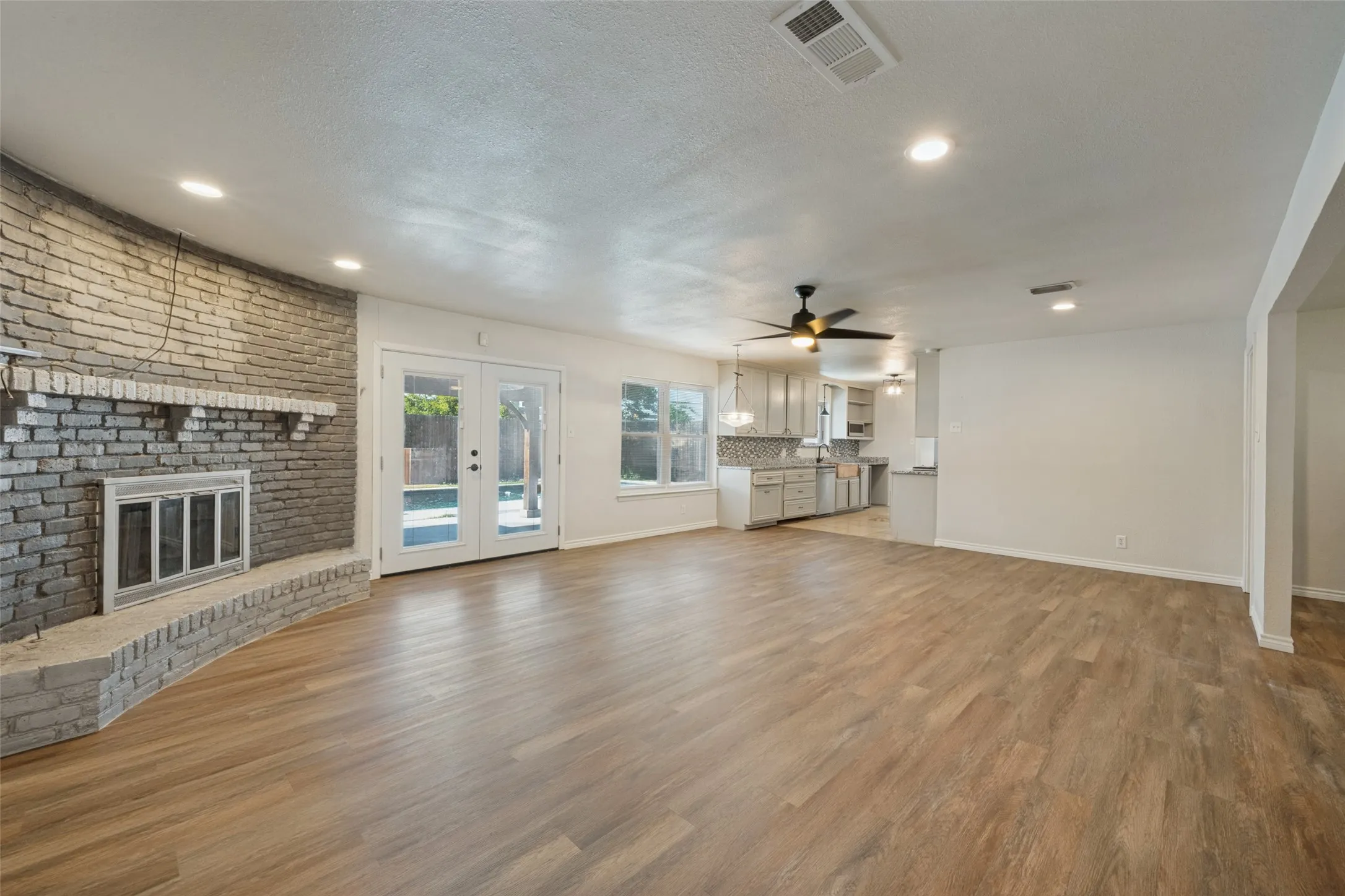 Expansive living area featuring wood-finish flooring, a brick fireplace, recessed lighting, and French doors