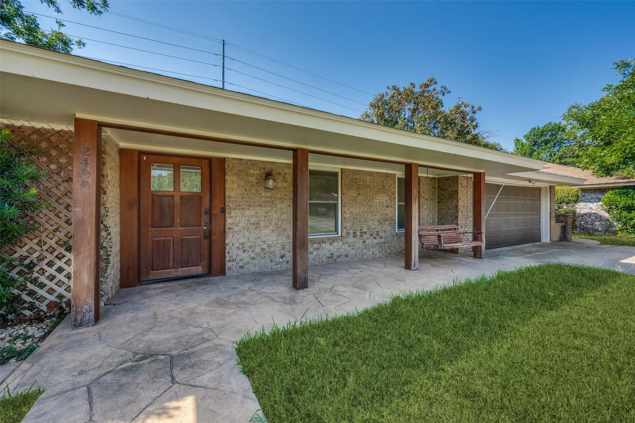 Brick exterior featuring a covered entry, wood-paneled front door with glass inserts, and a stamped concrete walkway