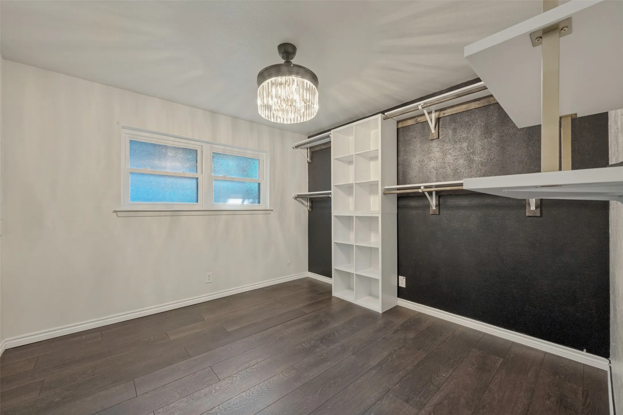 Dark wood-finish flooring, a contemporary ceiling light fixture, white built-in shelving, and white trim