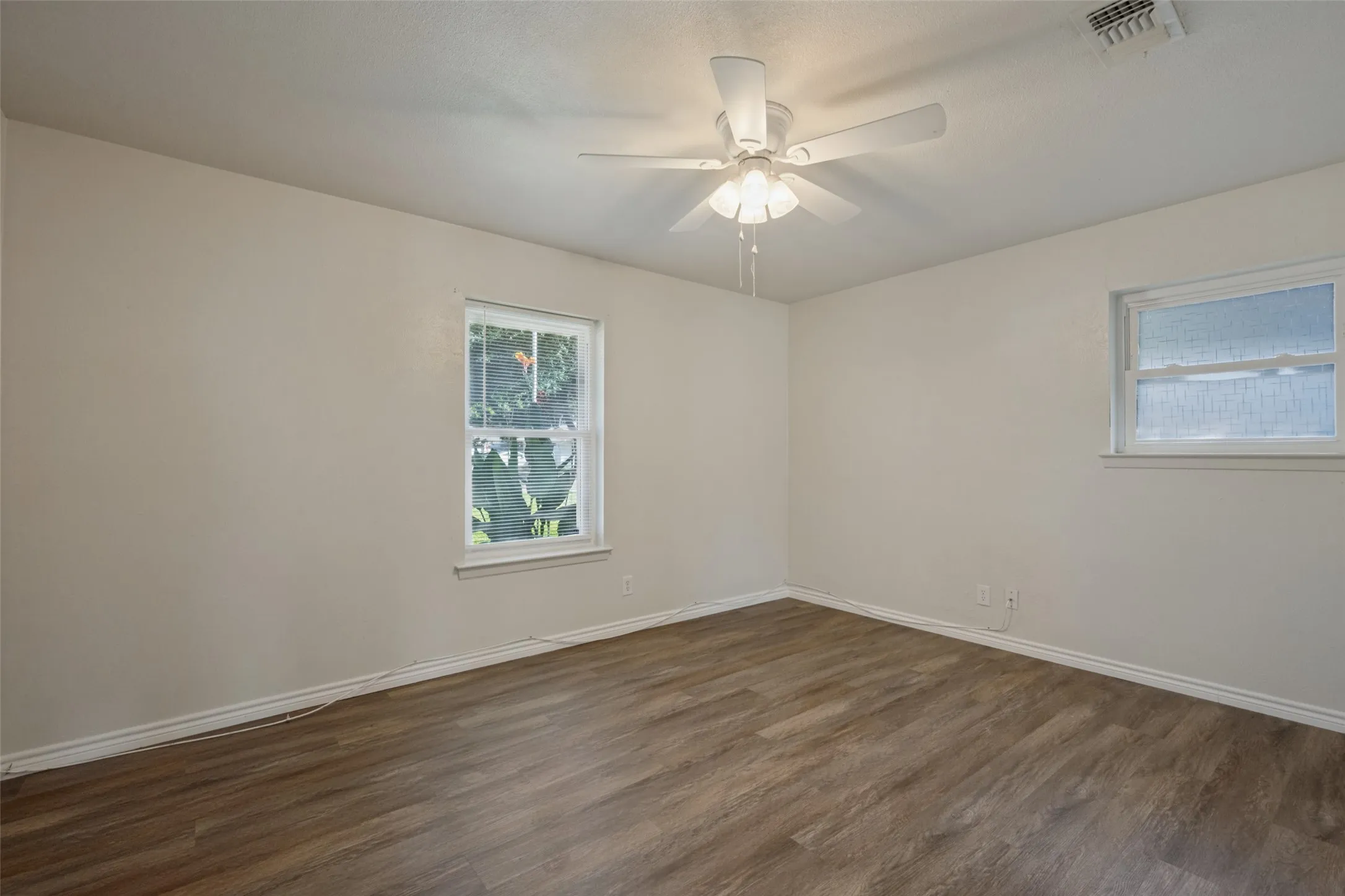 Neutral wall tones, wood-finish flooring, two windows, and a ceiling fan with integrated lighting