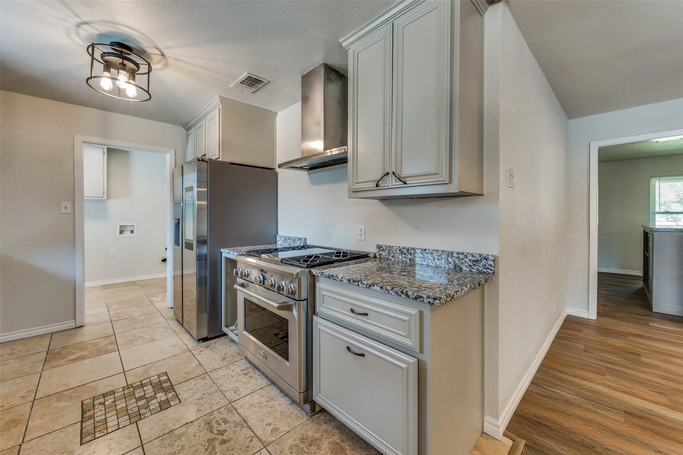 Kitchen featuring stainless steel appliances, light-toned cabinetry, patterned stone countertops, and tile flooring with a decorative inlay