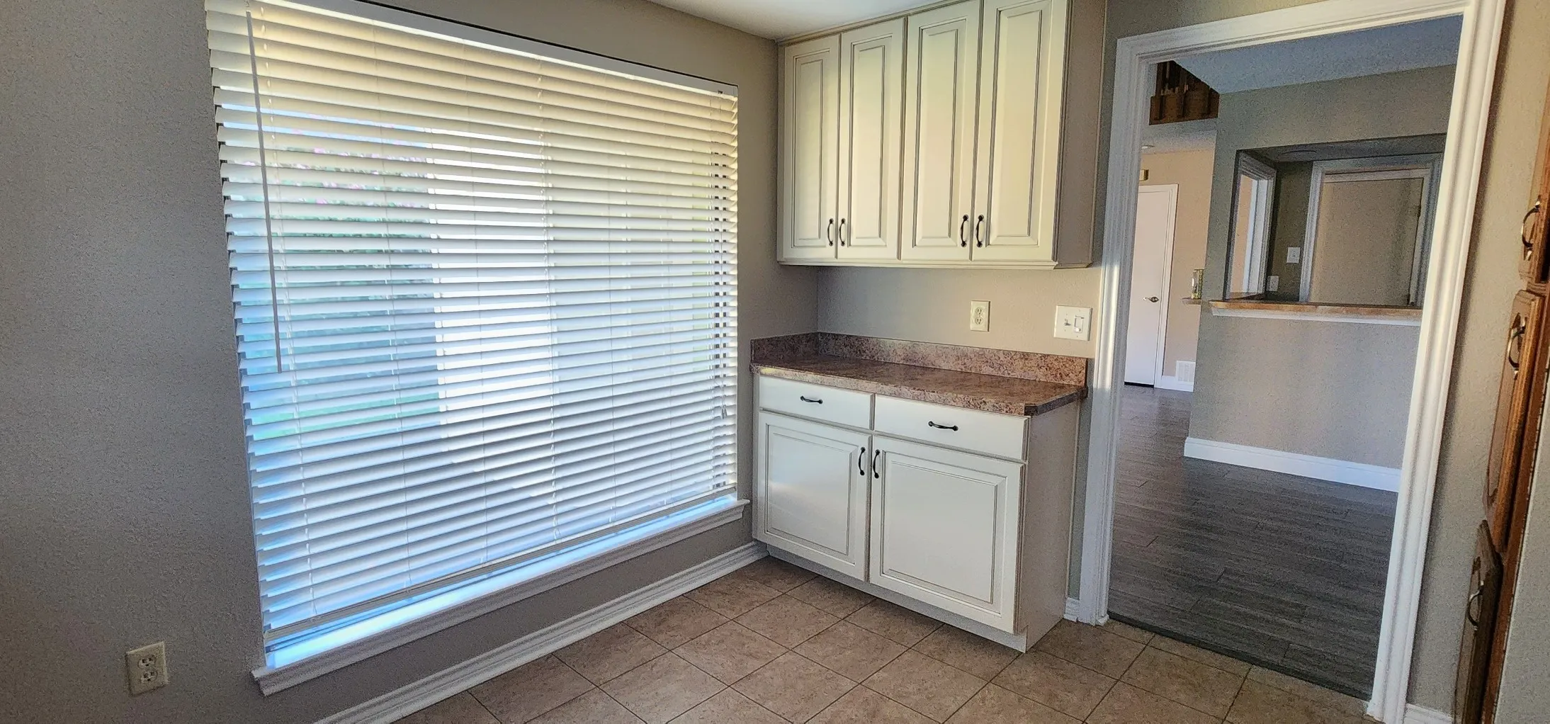 Tile flooring, white cabinetry with dark hardware, and a stone-finish countertop