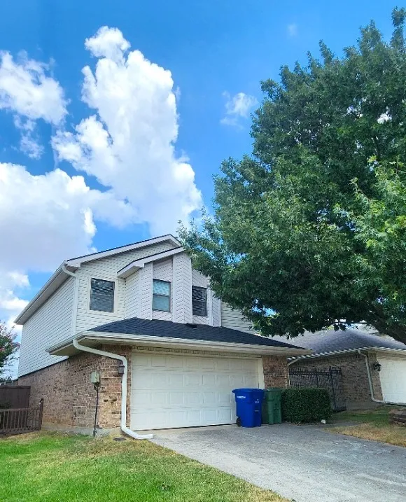 Two-story exterior featuring brick and siding, attached two-car garage, and a mature tree