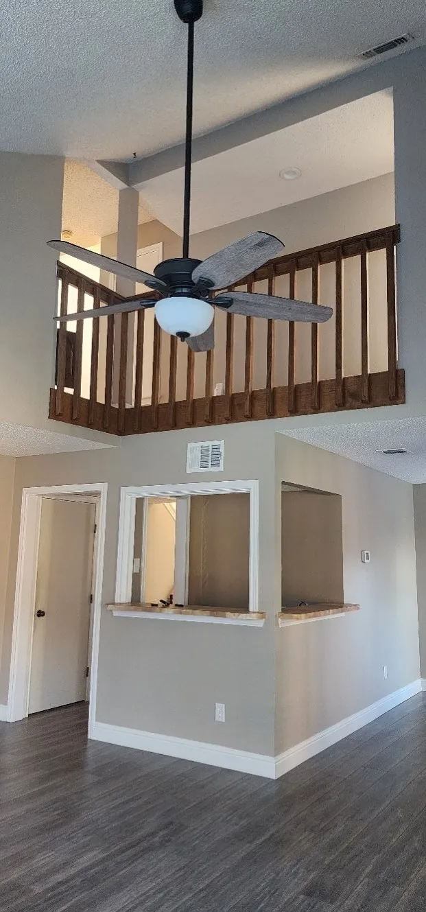 Wood-finish flooring, two-story ceiling, accent railing, and a pass-through opening