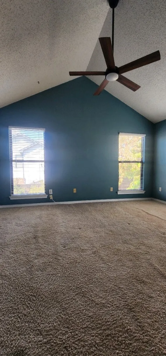 Vaulted ceiling with a ceiling fan, two windows with blinds, and wall-to-wall carpeting