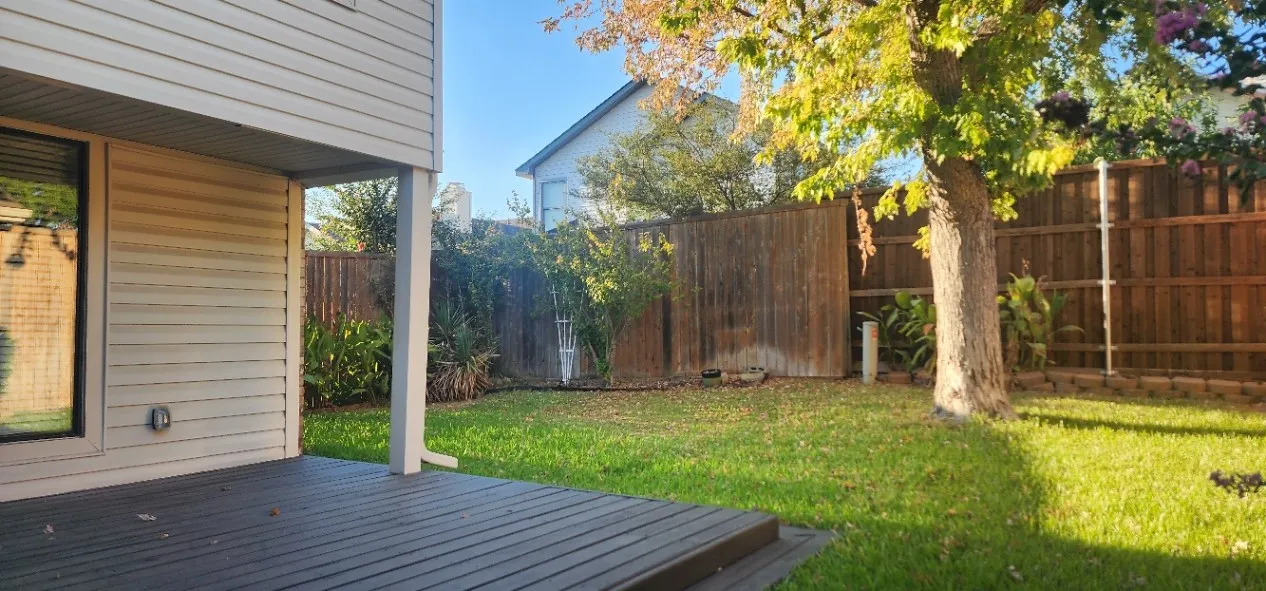 Expansive backyard featuring a wood privacy fence, mature tree, and green lawn