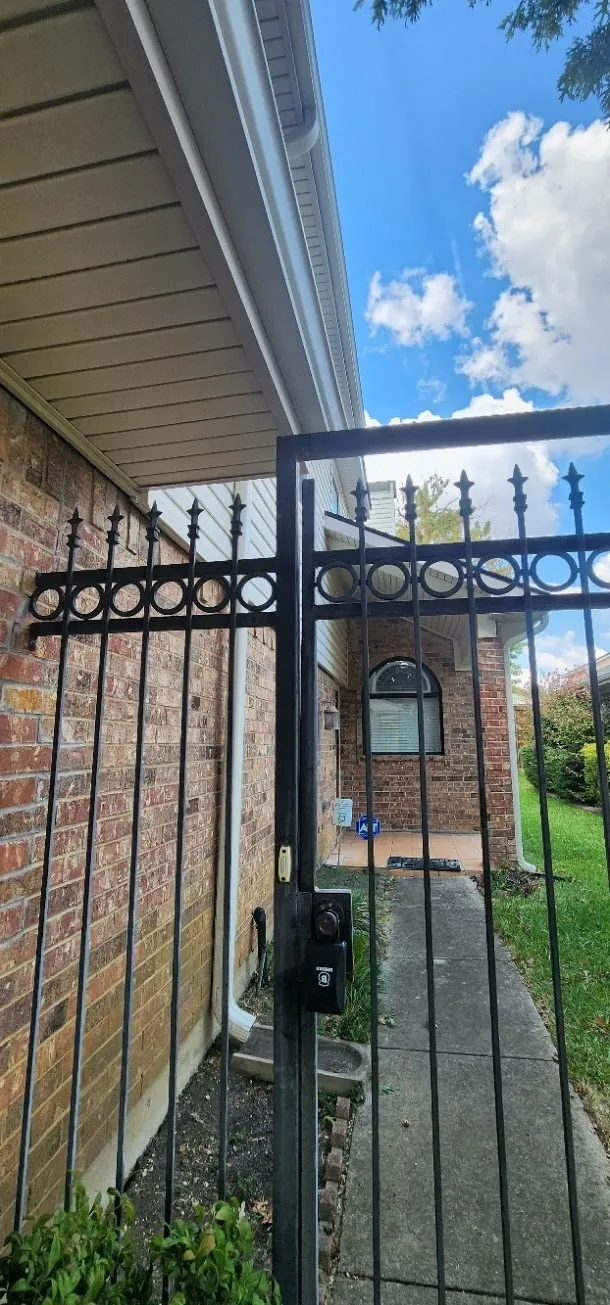Brick exterior with a decorative wrought iron gate and a concrete walkway