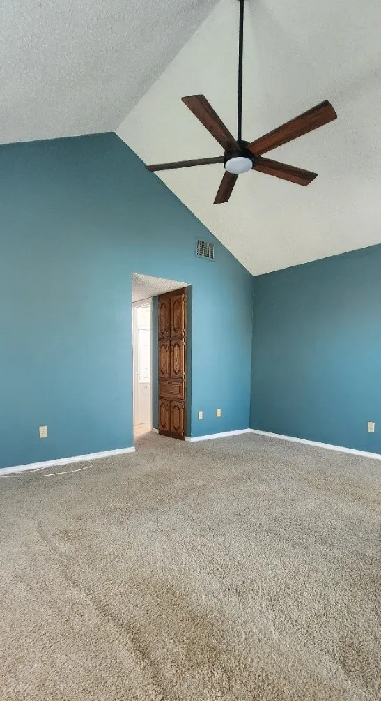 Vaulted ceiling with a five-blade ceiling fan, wall-to-wall carpeting, and wood-paneled bifold doors