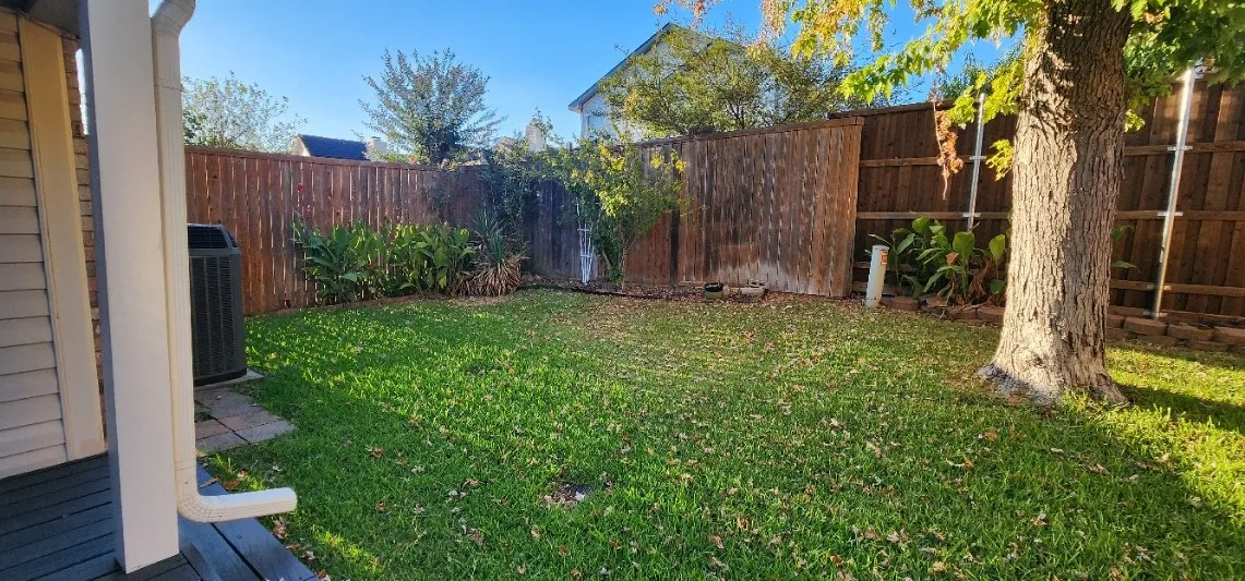 Expansive yard with natural grass, perimeter wood fencing, and mature trees