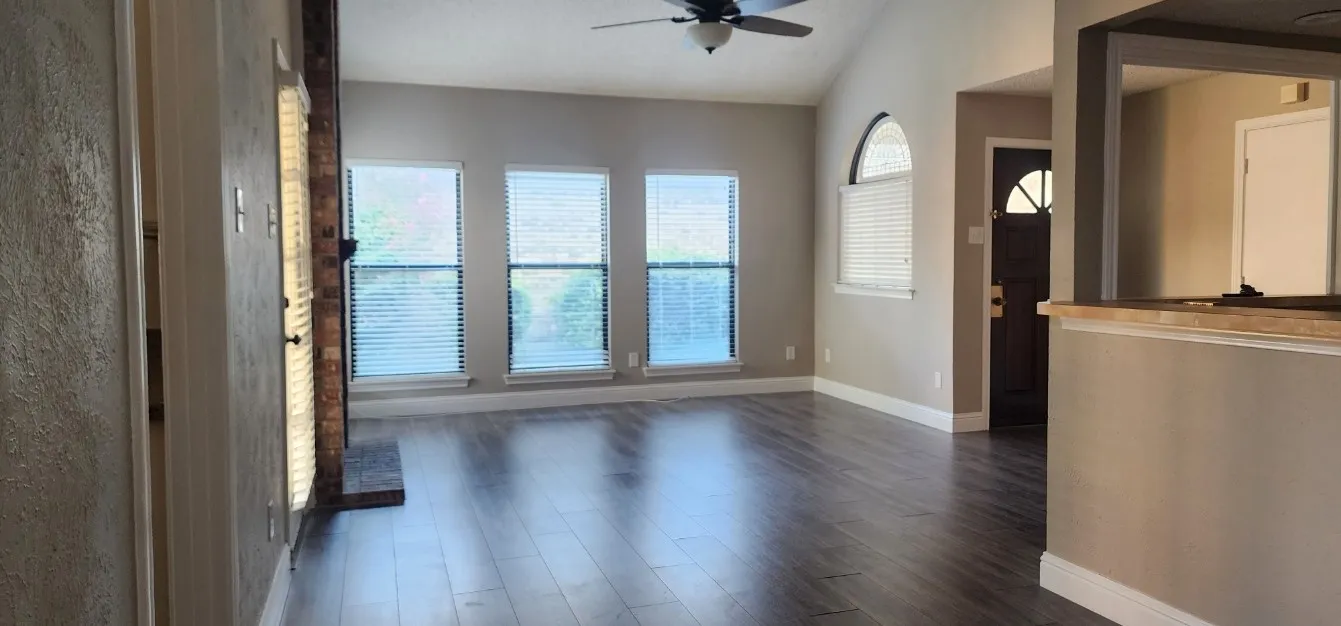 Vaulted ceiling with a ceiling fan, dark wood-finish flooring, three large windows, a brick fireplace, and an arched window
