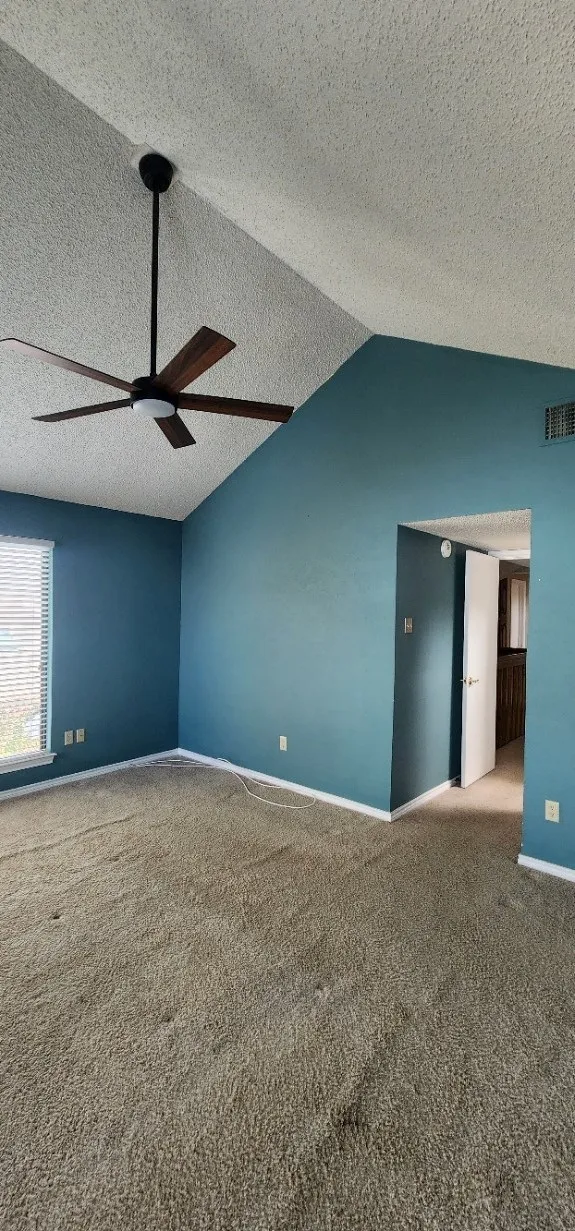 Vaulted ceiling with an attached ceiling fan, large window with blinds, and wall-to-wall carpeting