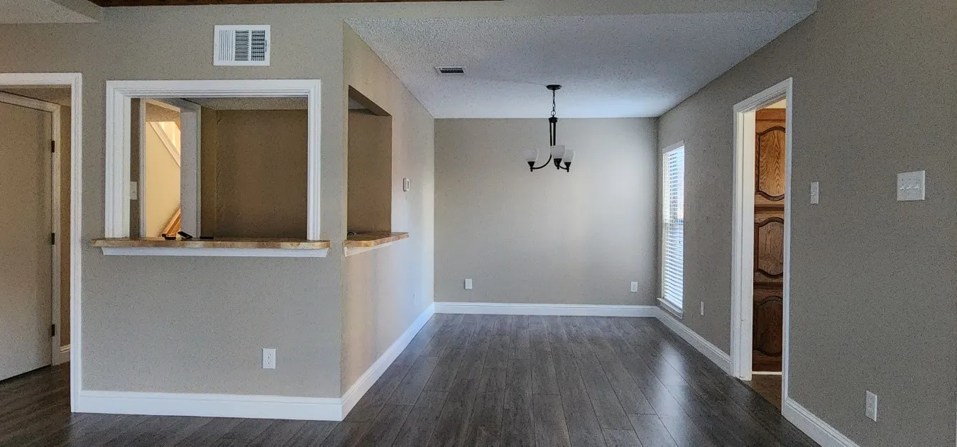 Wood-finish flooring, neutral wall tones, pass-through window with counter, white trim, and a contemporary chandelier