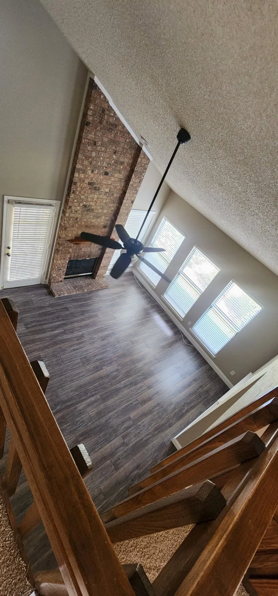 Two-story living area featuring wood-finish flooring, a brick fireplace, a ceiling fan, and multiple windows