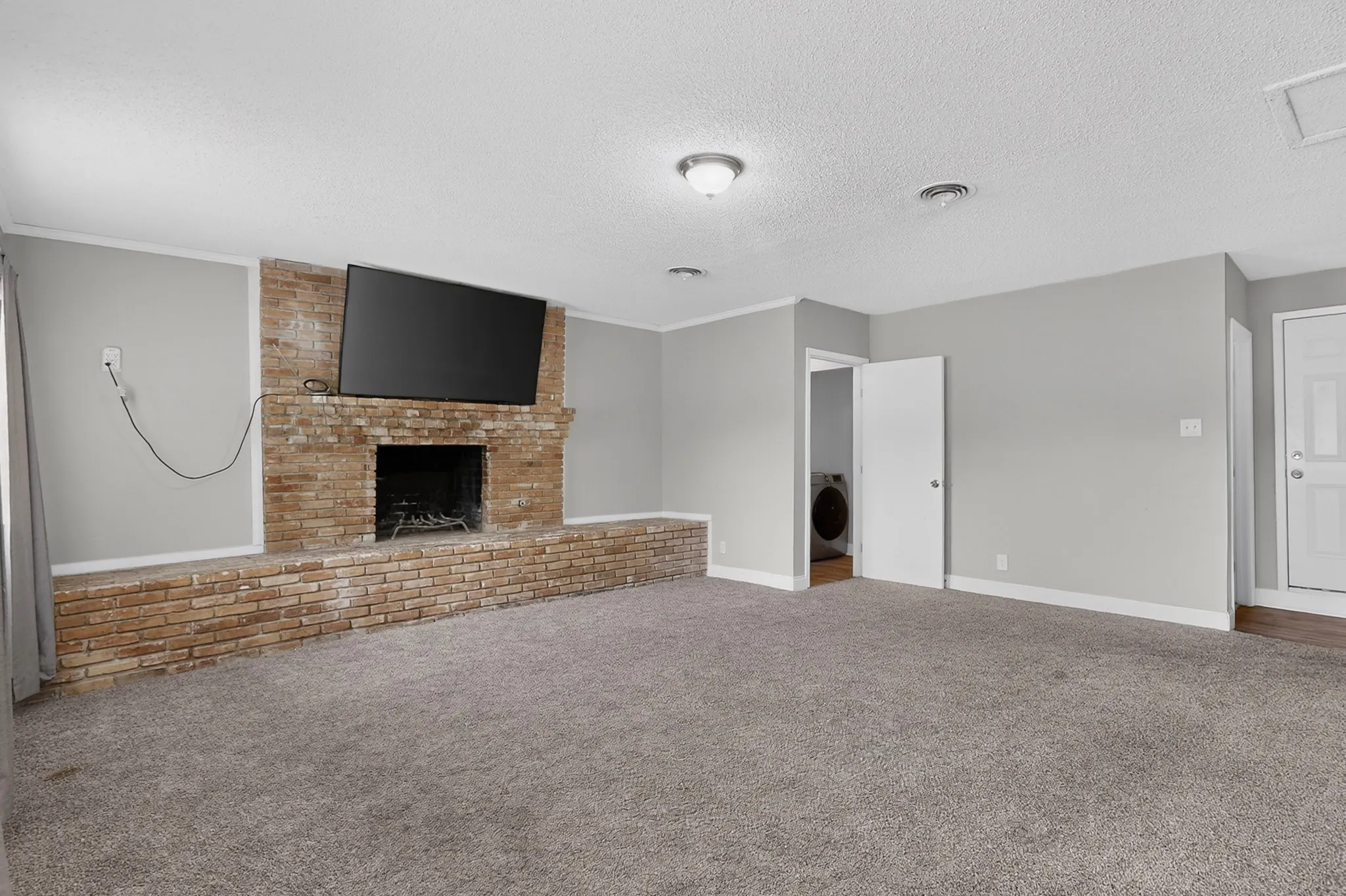 Brick fireplace with hearth, plush carpet flooring, recessed lighting, and a solid entry door