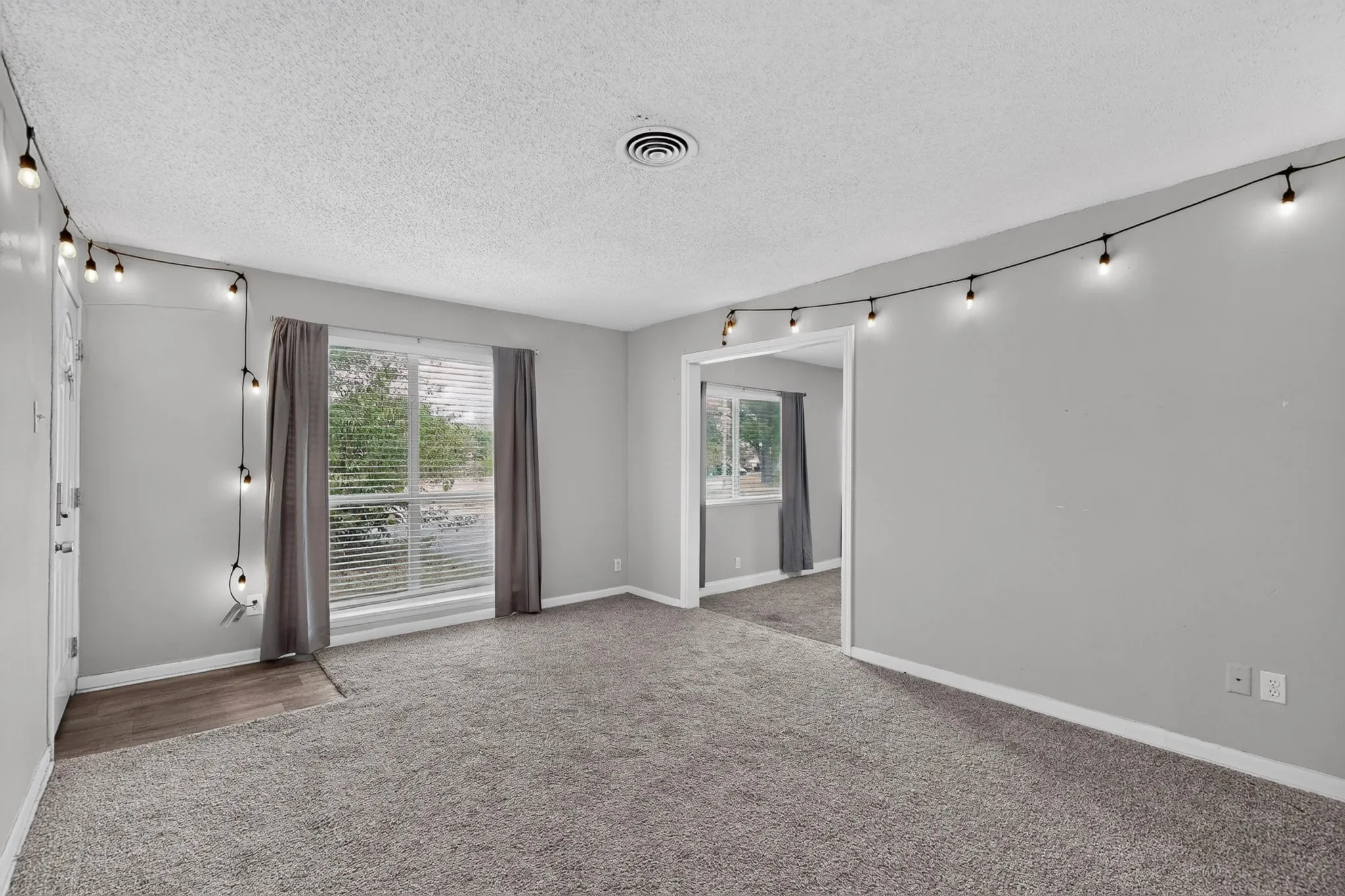 Carpeted flooring, neutral wall color, window with blinds and drapes, wood-finish flooring at entry