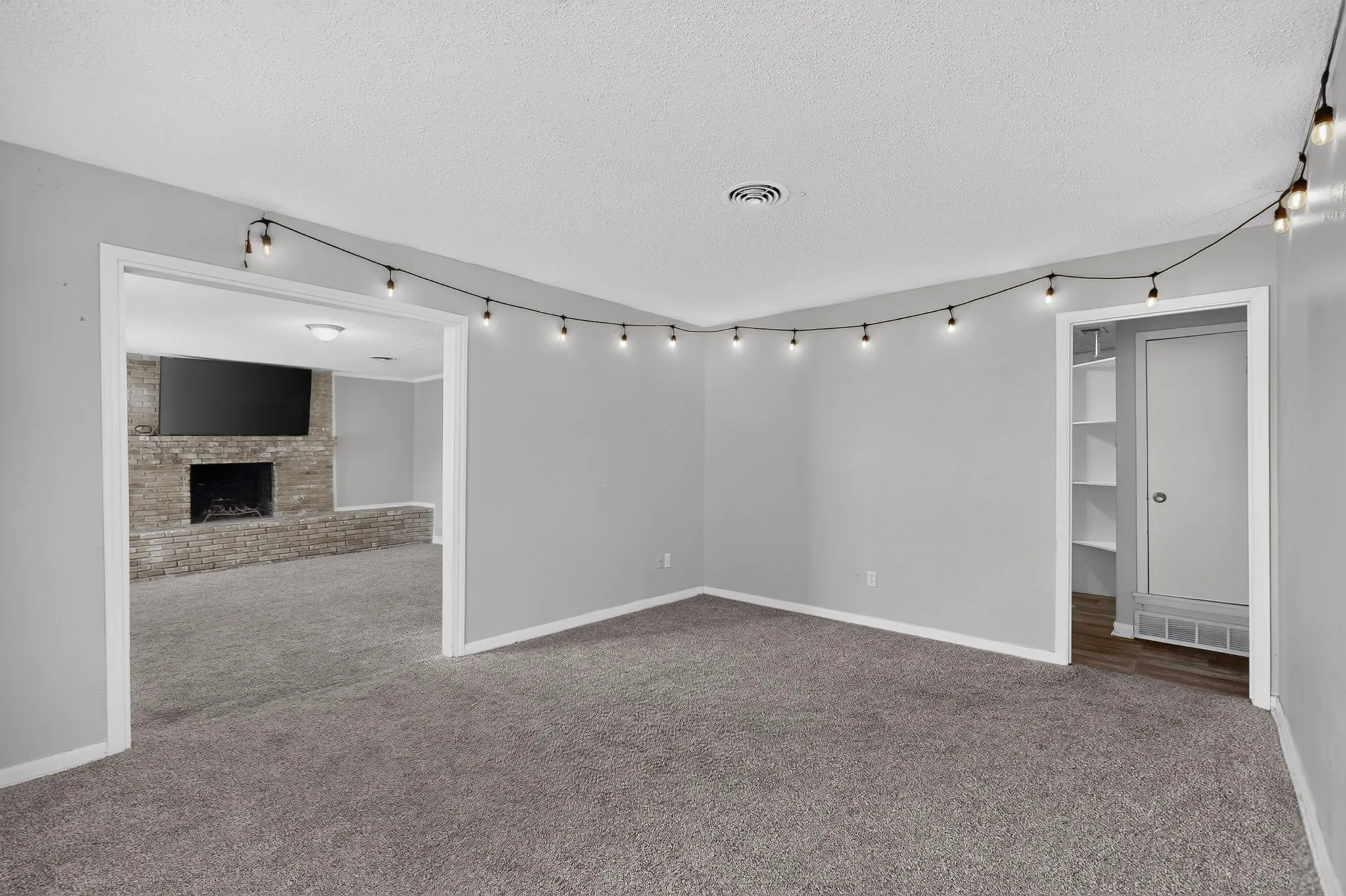 Spacious carpeted room with light grey walls and a built-in closet featuring shelving