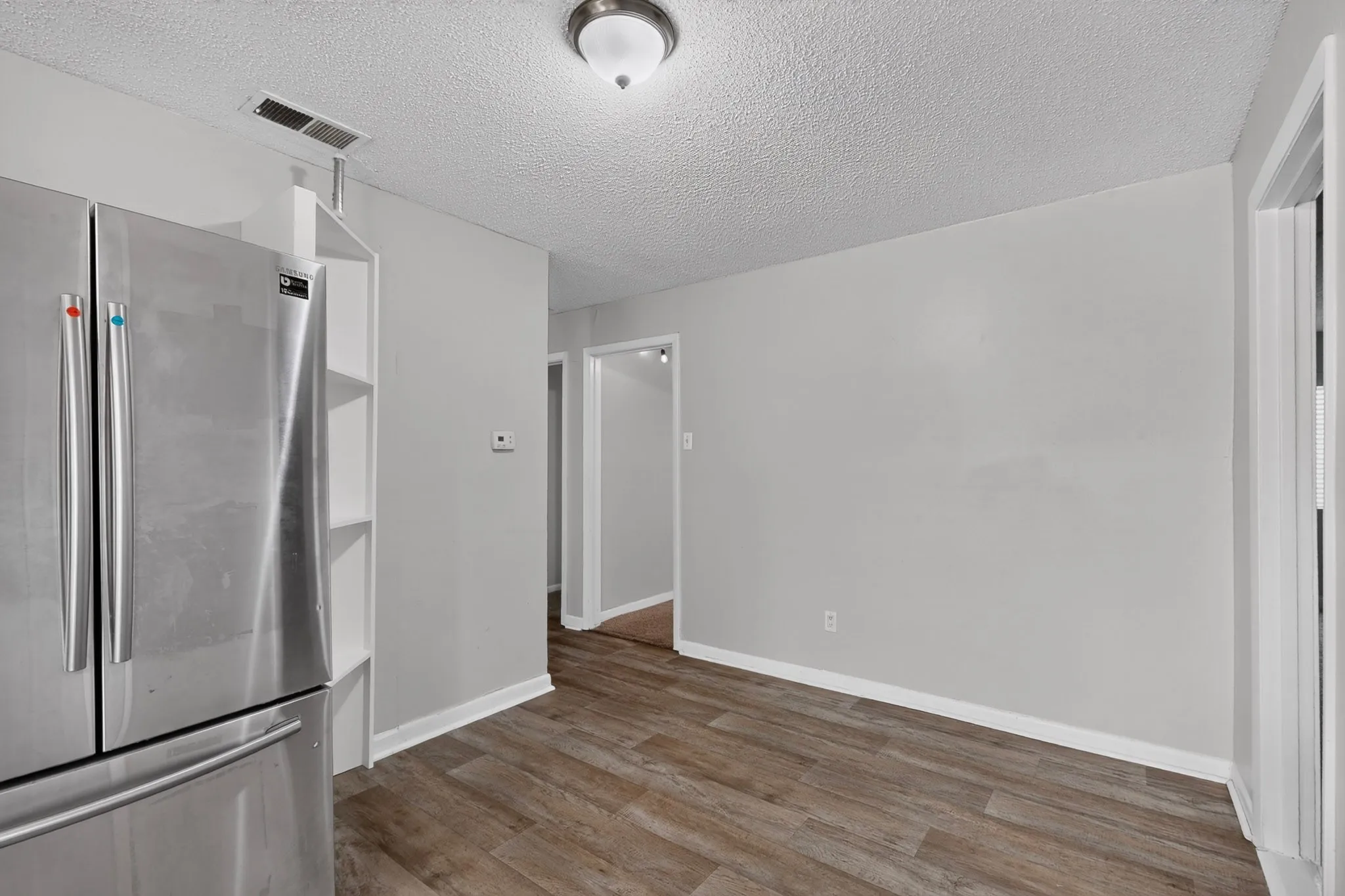 Stainless steel refrigerator, wood-finish flooring, recessed shelving, neutral wall paint, and white trim