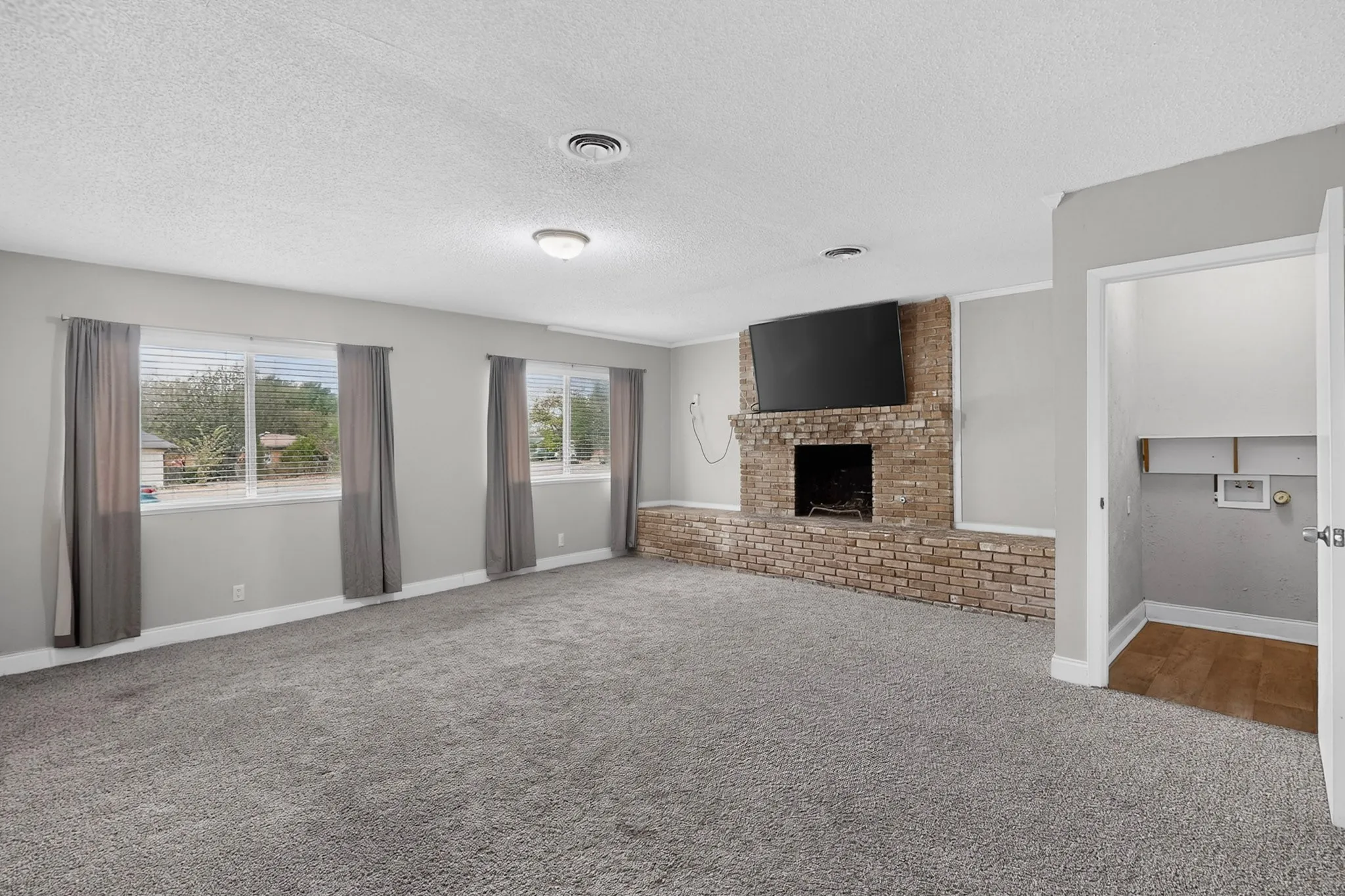 Spacious living area featuring light gray carpet, a brick fireplace, and multiple windows