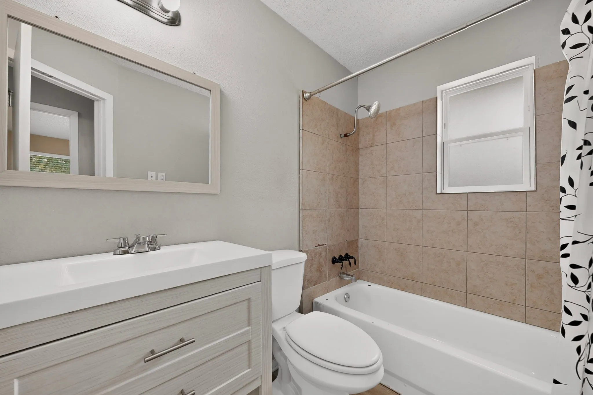 Bathroom featuring a wood-finish vanity with a single basin sink, brushed nickel faucet, framed mirror, and a white bathtub with subway tile surround